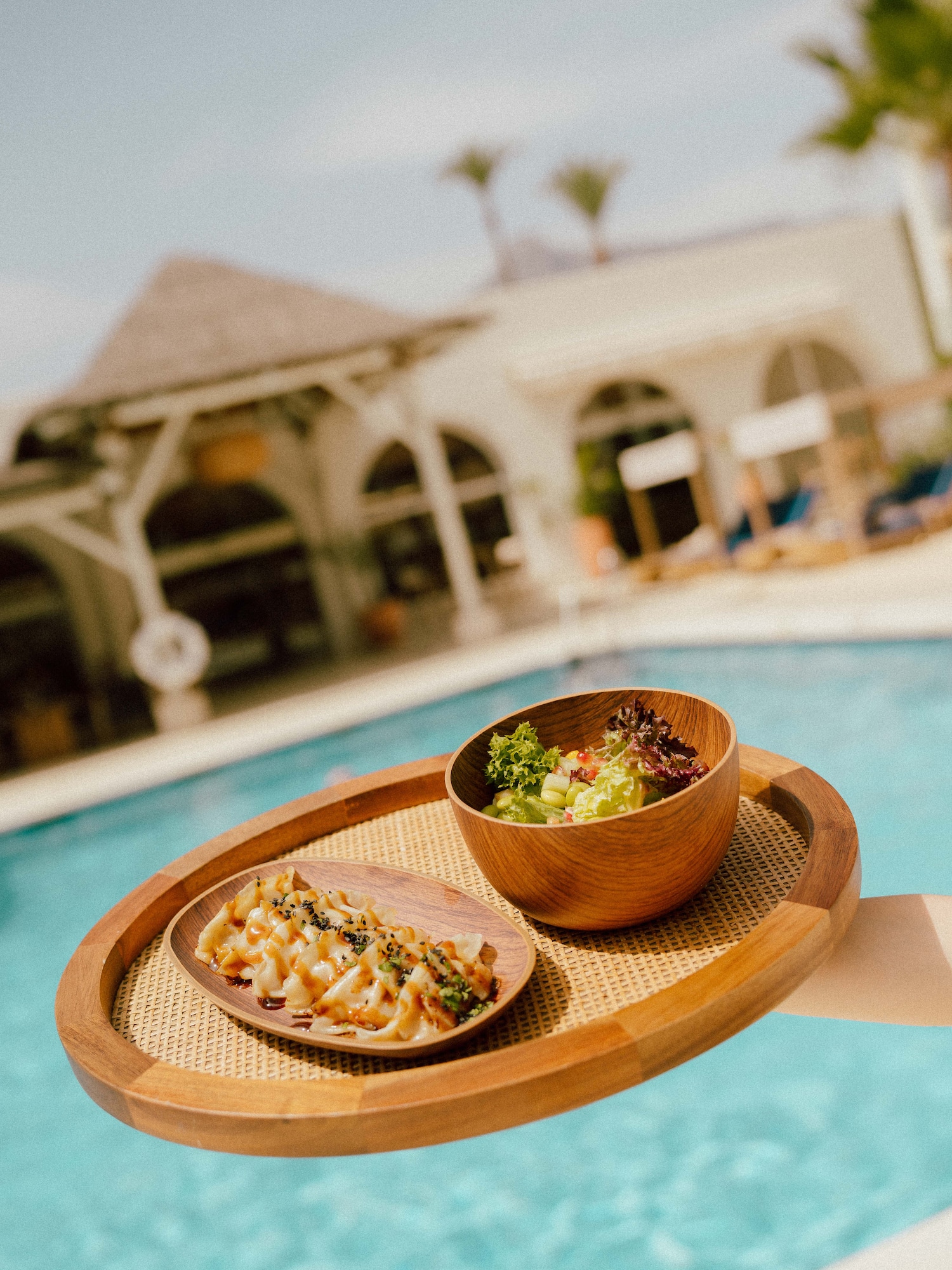 Resort poolside dining with gyoza and fresh salad on a woven tray.