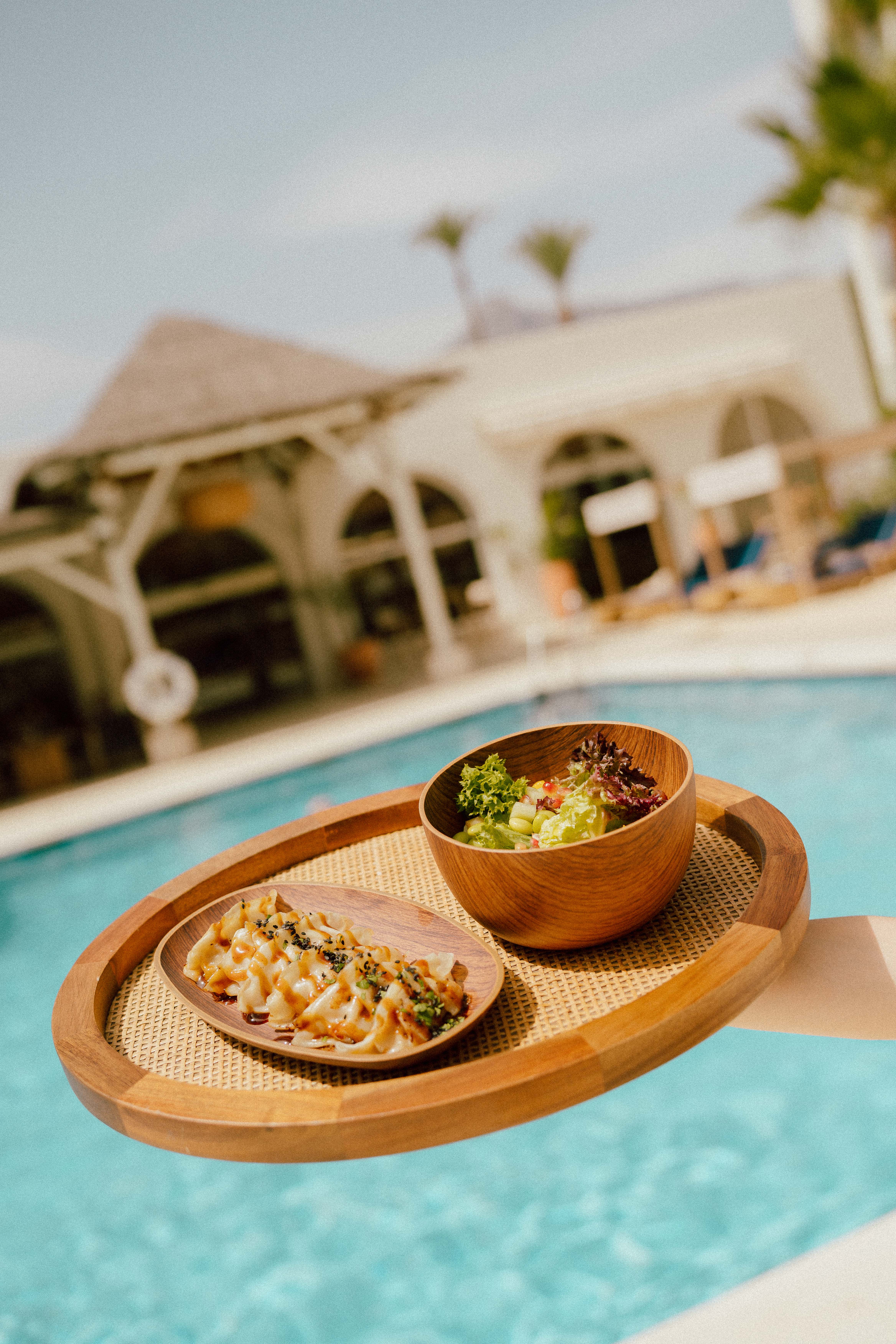 Resort poolside dining with gyoza and fresh salad on a woven tray.