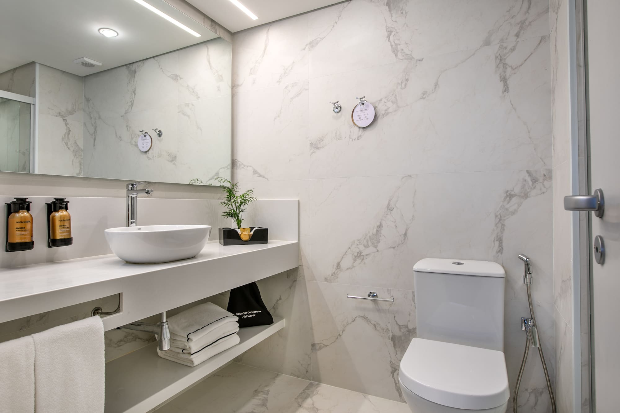 Modern hotel bathroom with white marble walls, vanity, vessel sink, and toilet.