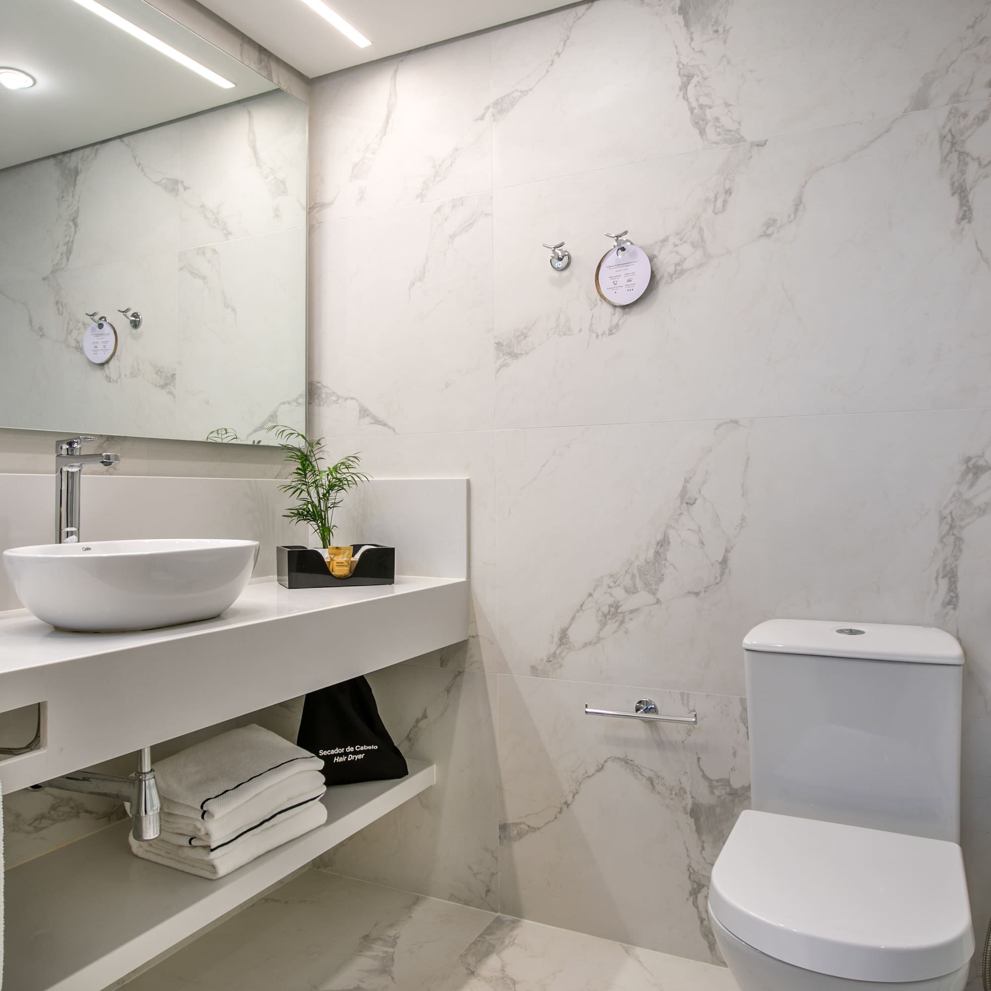 Modern hotel bathroom with white marble walls, vanity, vessel sink, and toilet.