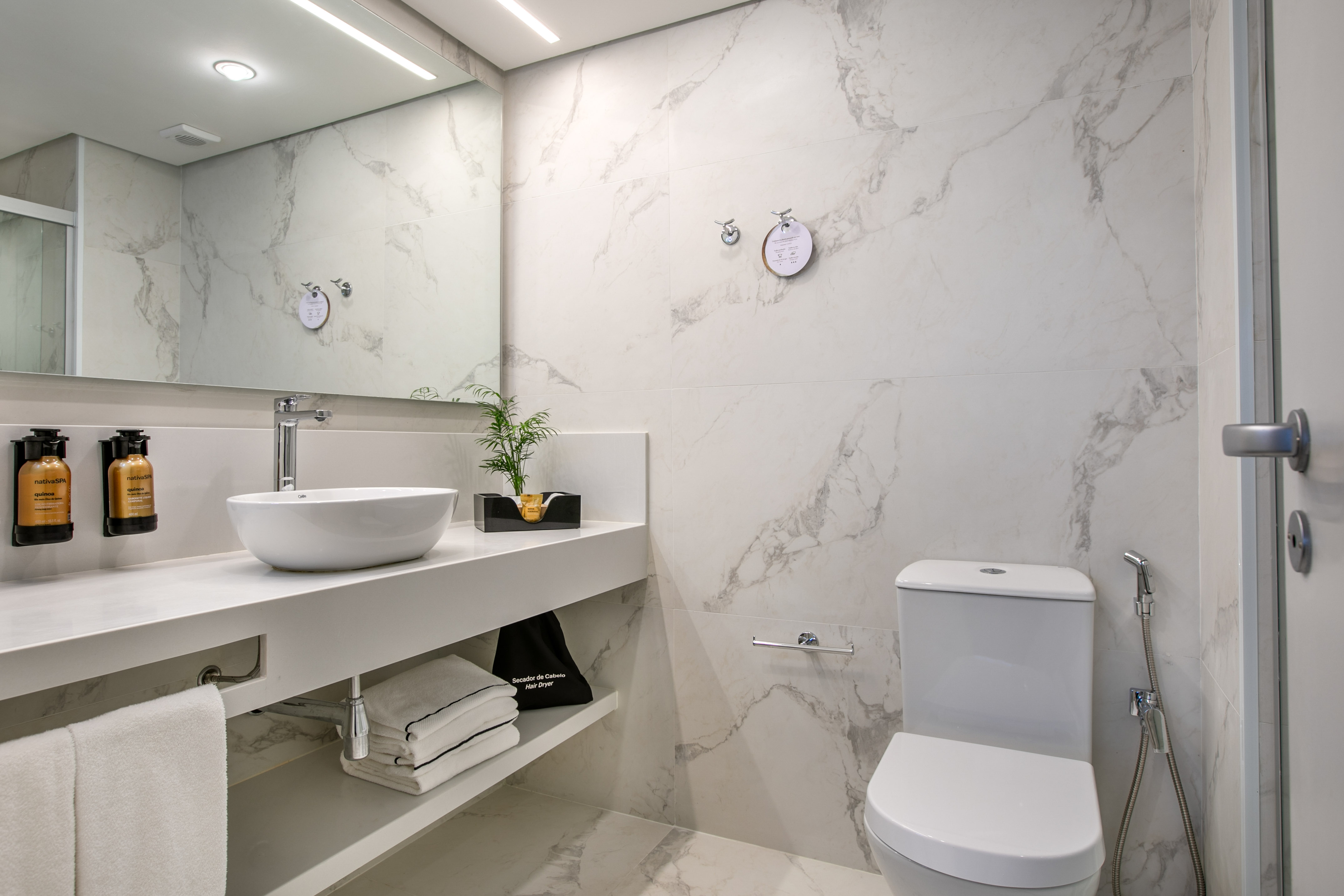 Modern hotel bathroom with white marble walls, vanity, vessel sink, and toilet.