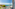 Sunny balcony overlooking turquoise sea and coastal marina with boats.