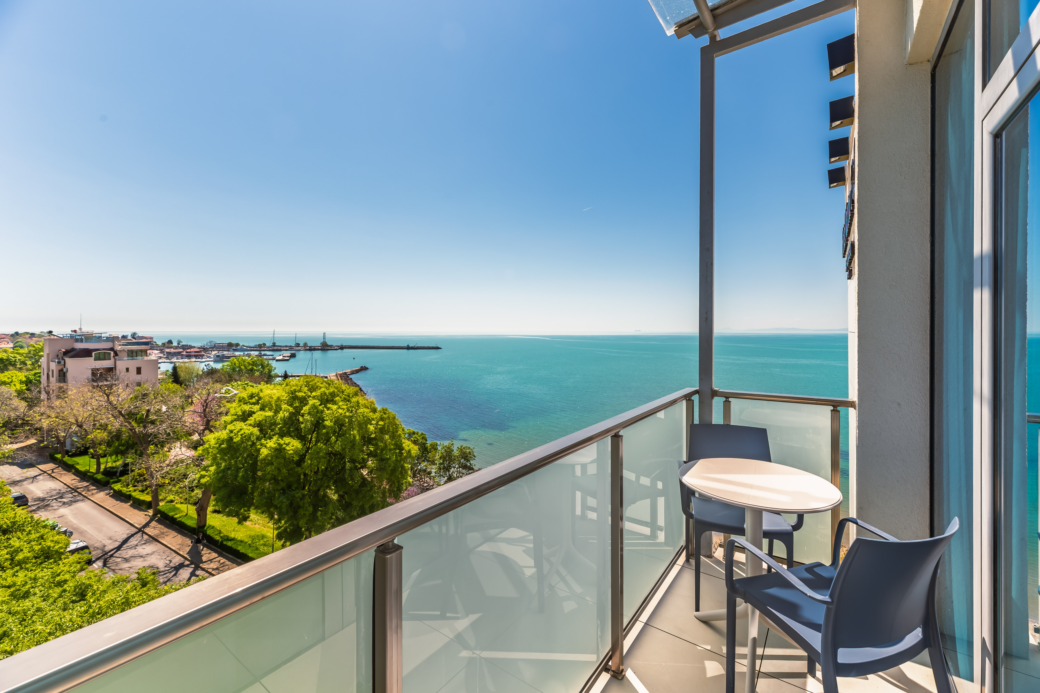 Sunny balcony overlooking turquoise sea and coastal marina with boats.