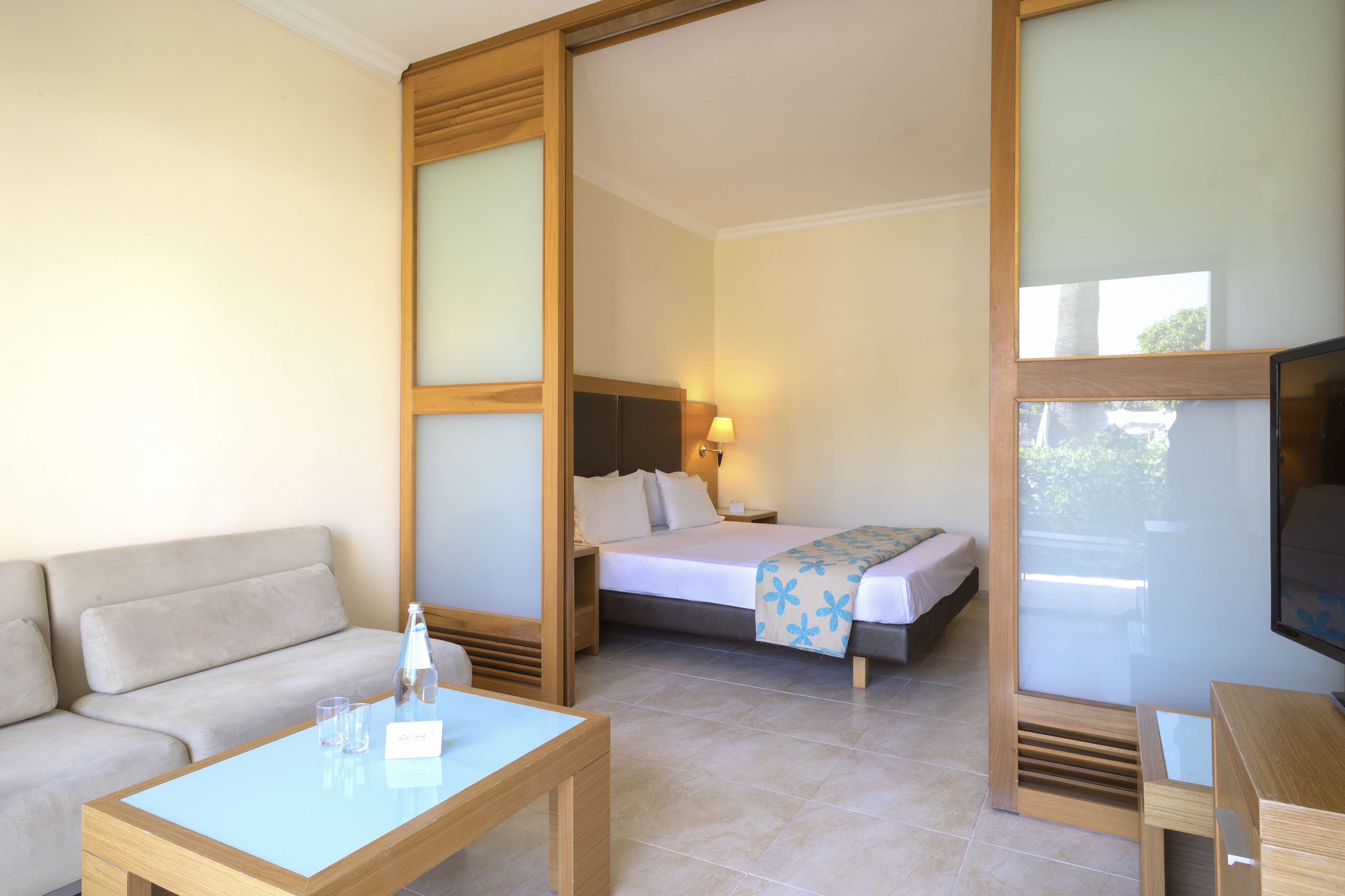 Hotel suite with sofa, coffee table, and bed separated by wooden sliding door.