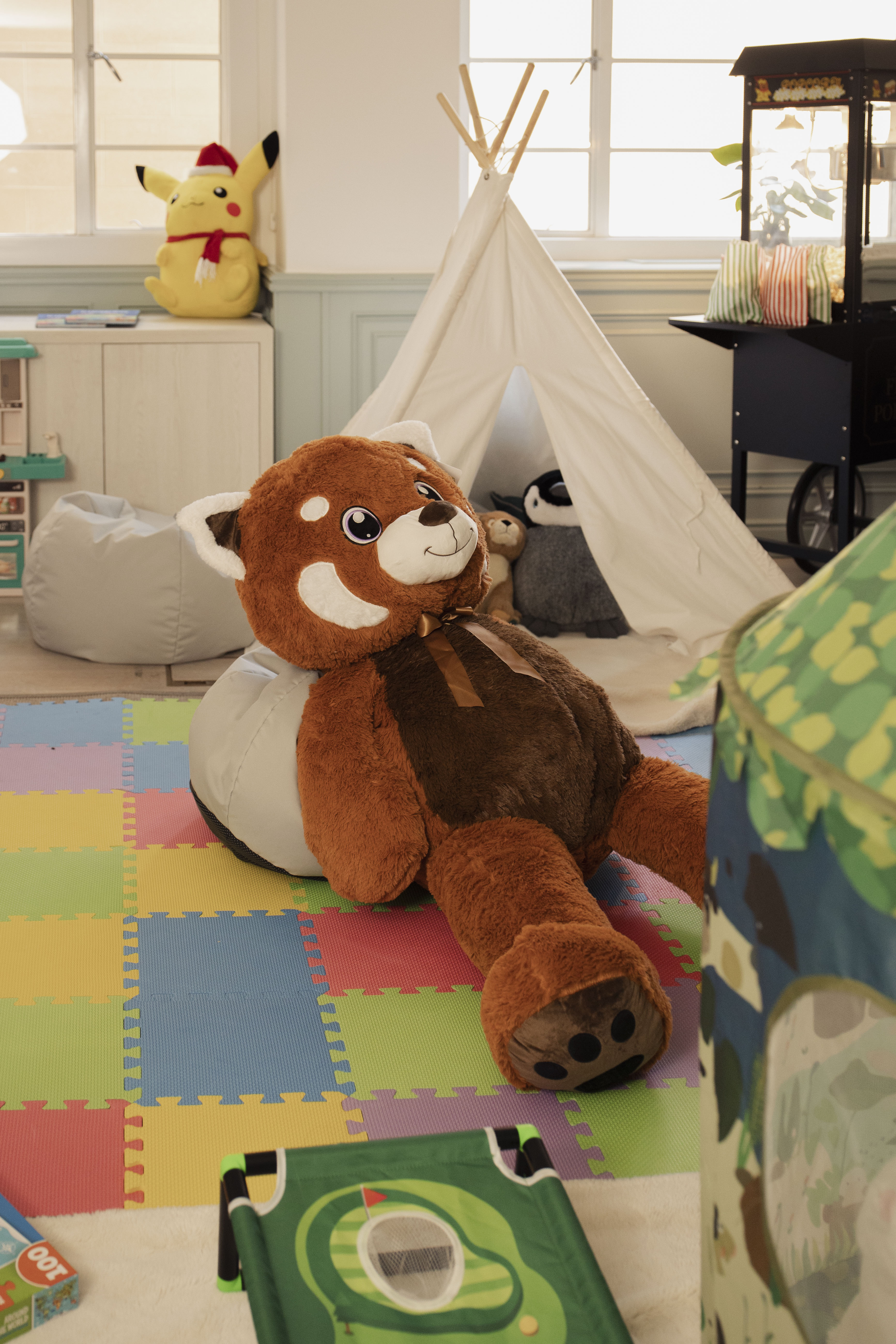 Large red panda plush toy in a colorful kids' playroom with teepee and toys.