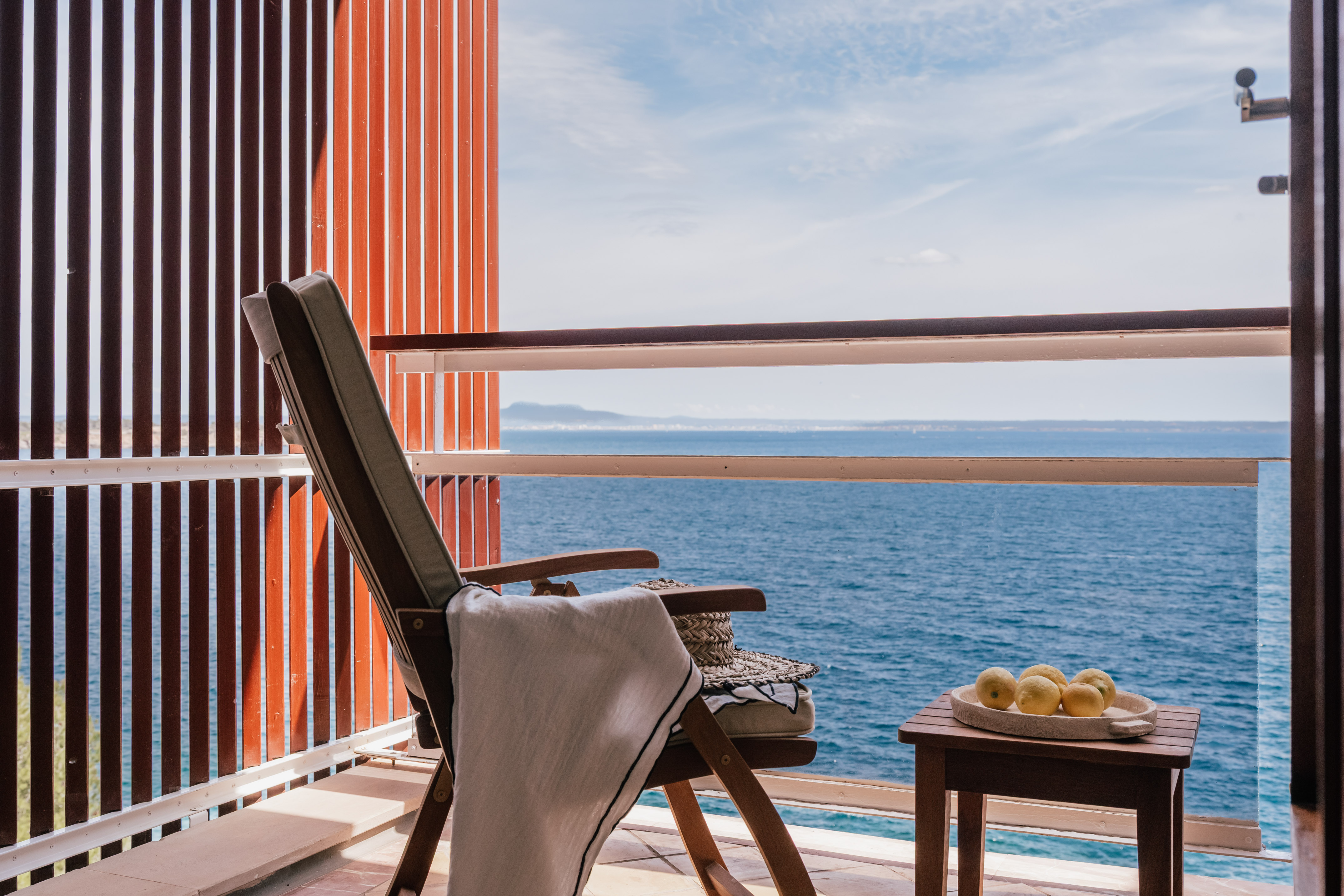 Relaxing balcony with chair, straw hat, lemons, and ocean view.