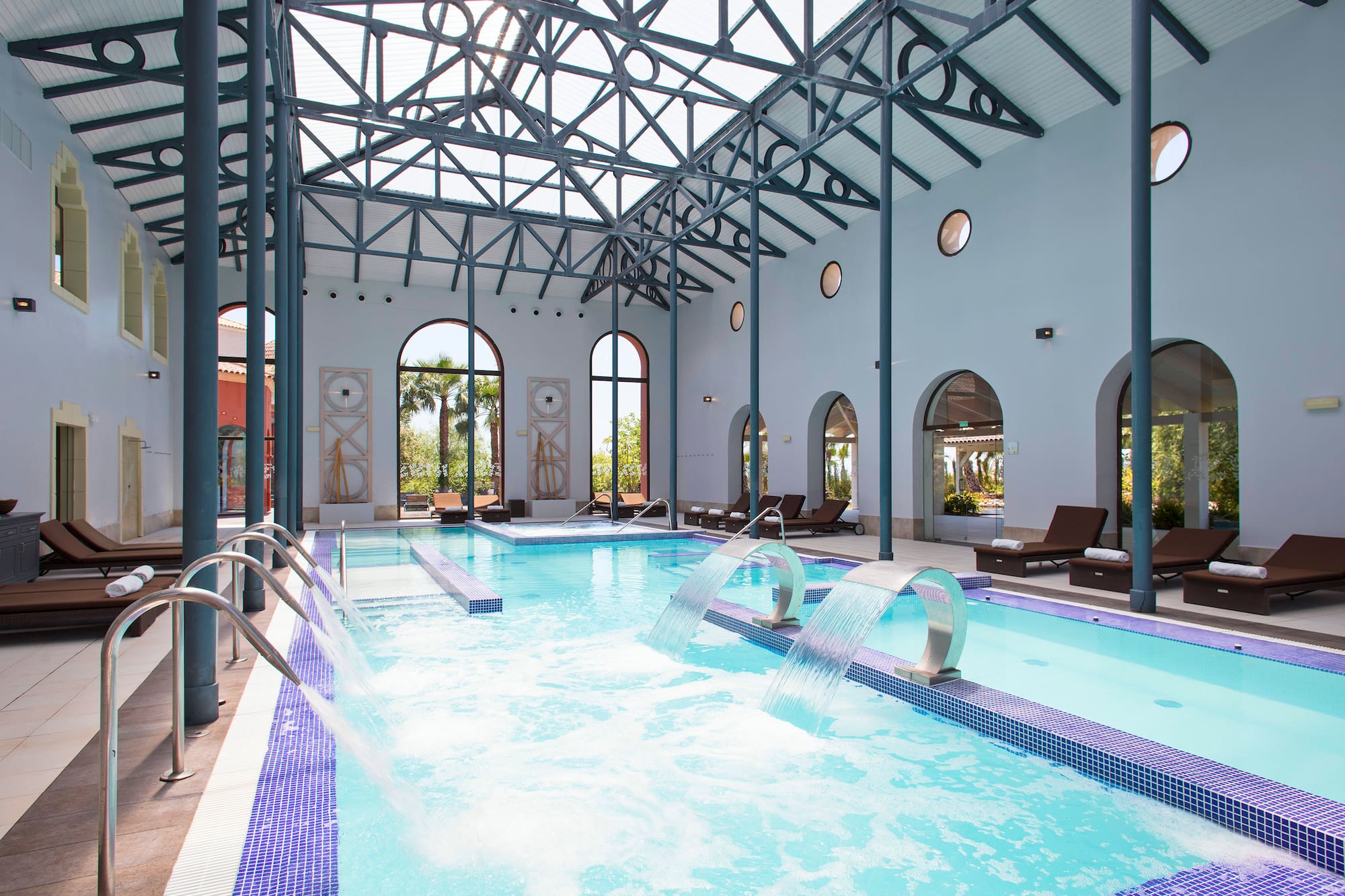 Indoor spa pool with waterfall features, vaulted ceiling, and arched windows.