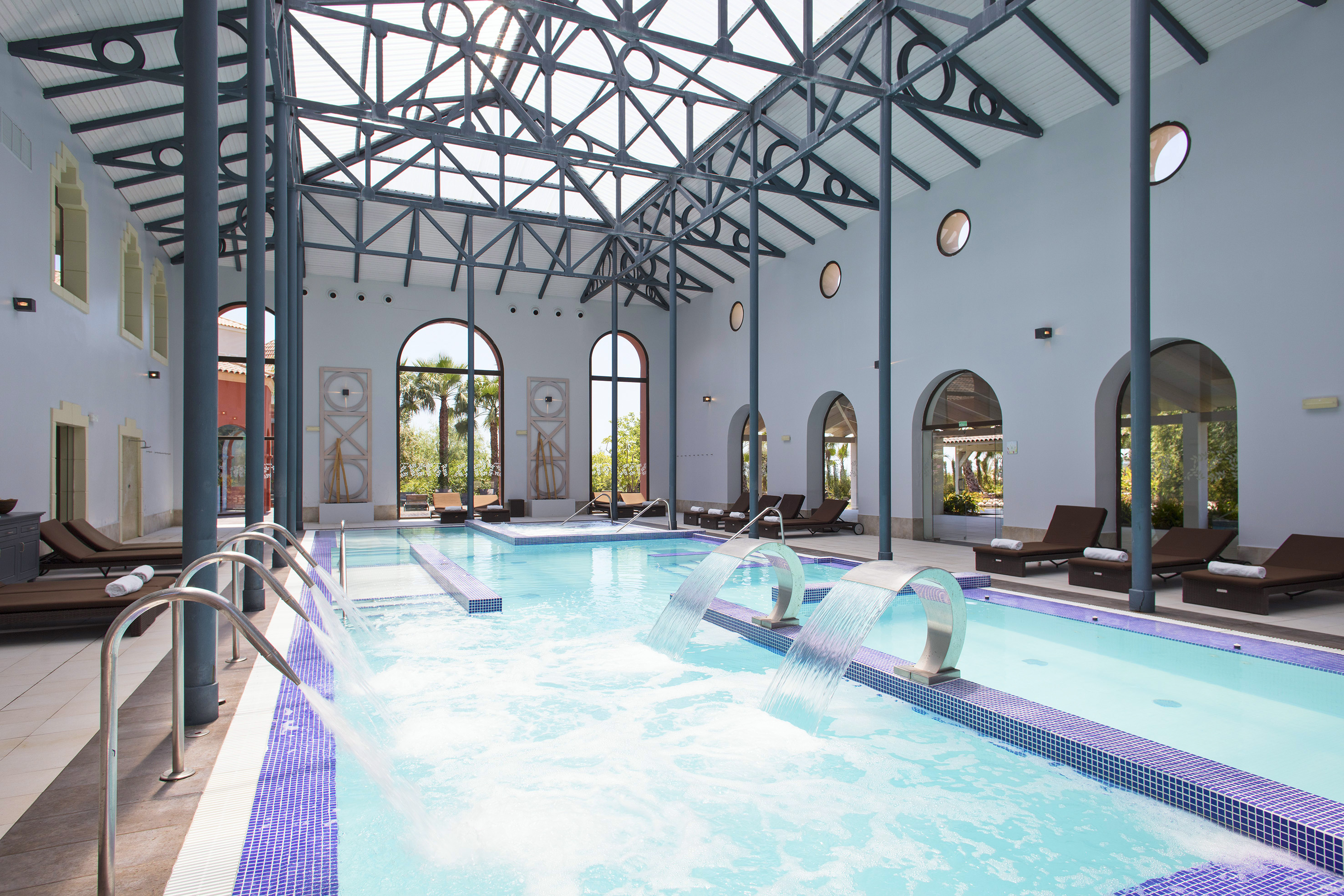 Indoor spa pool with waterfall features, vaulted ceiling, and arched windows.