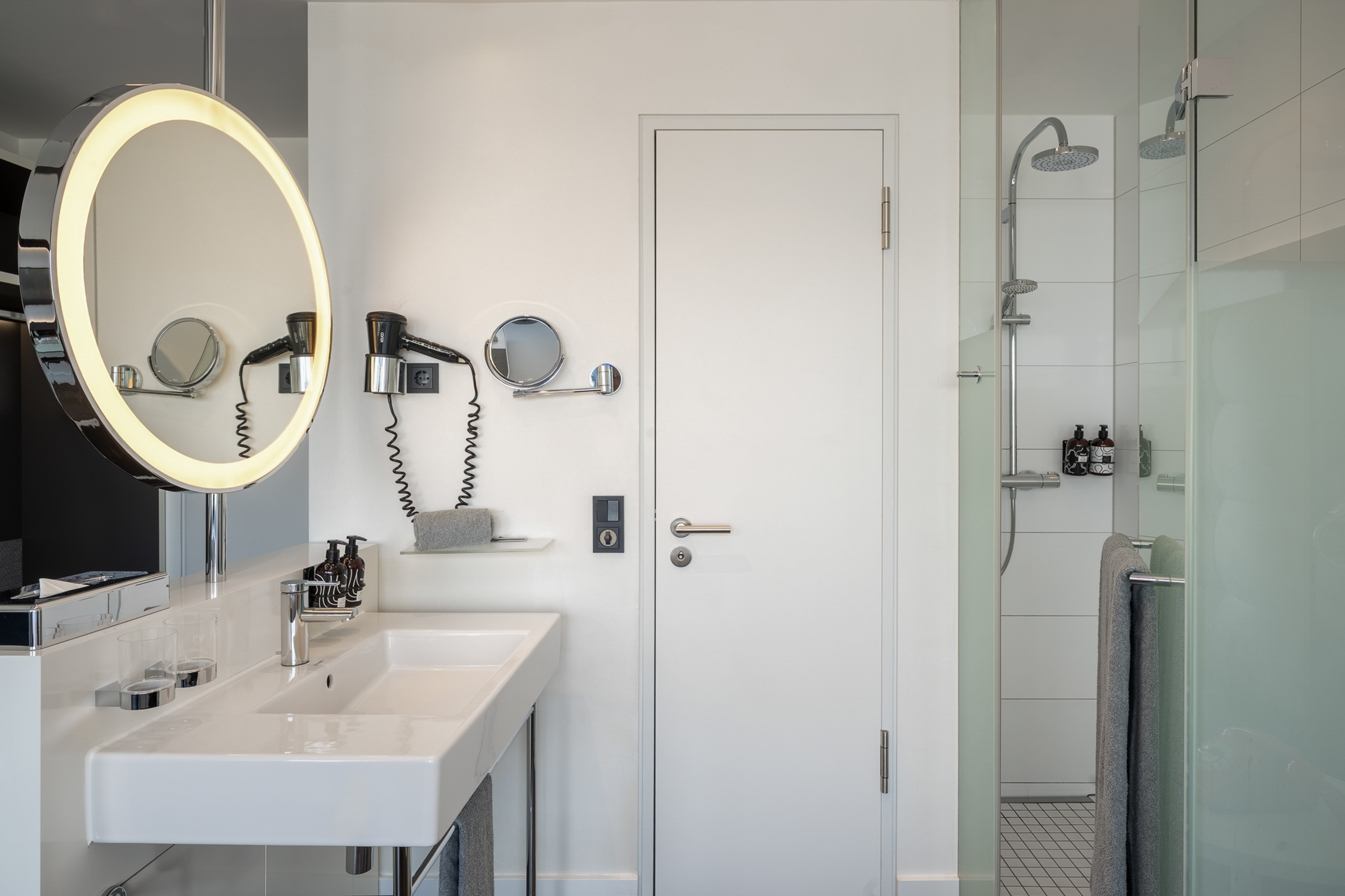 Modern hotel bathroom with illuminated mirror, white sink, and glass shower.