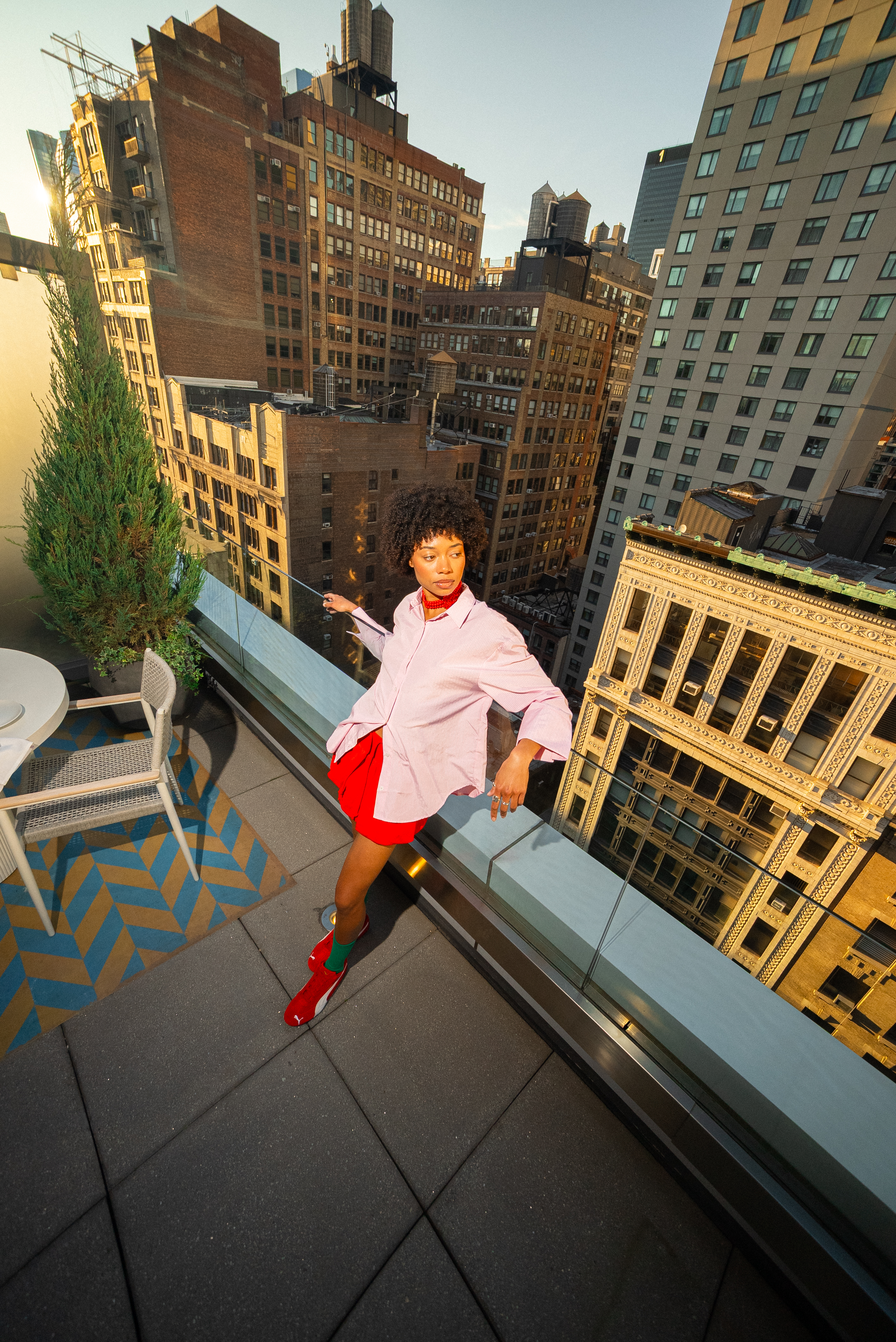 Person in pink shirt, red shorts on NYC rooftop, overlooking city skyline.