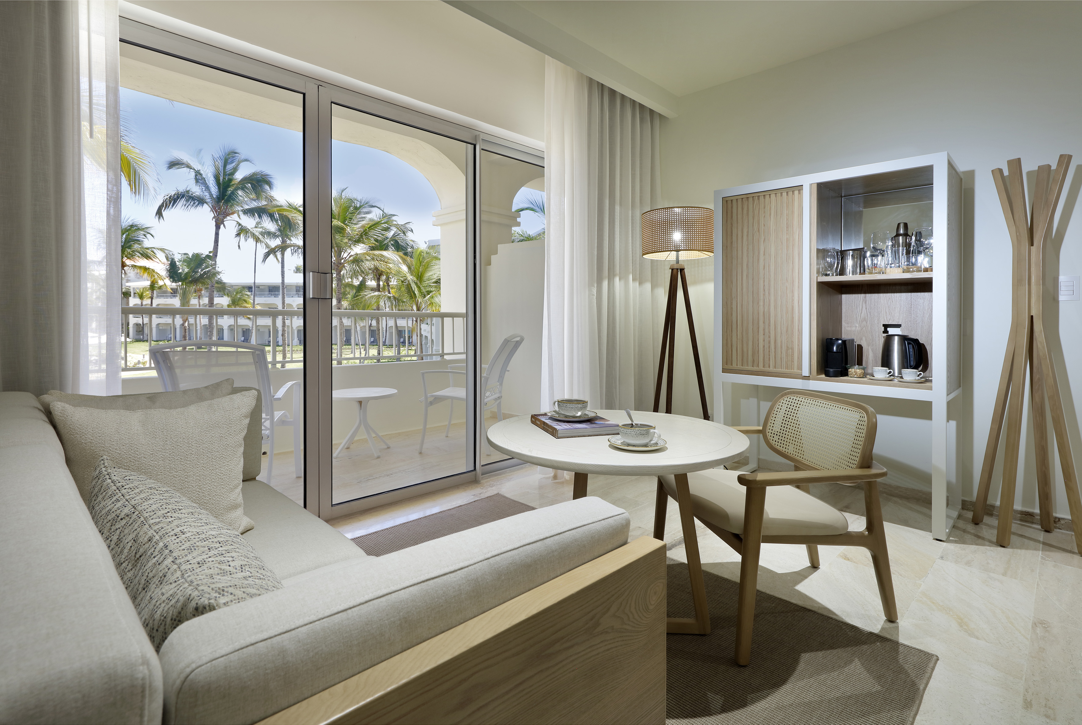 Modern resort suite with balcony, tropical palm trees, and bright living area.