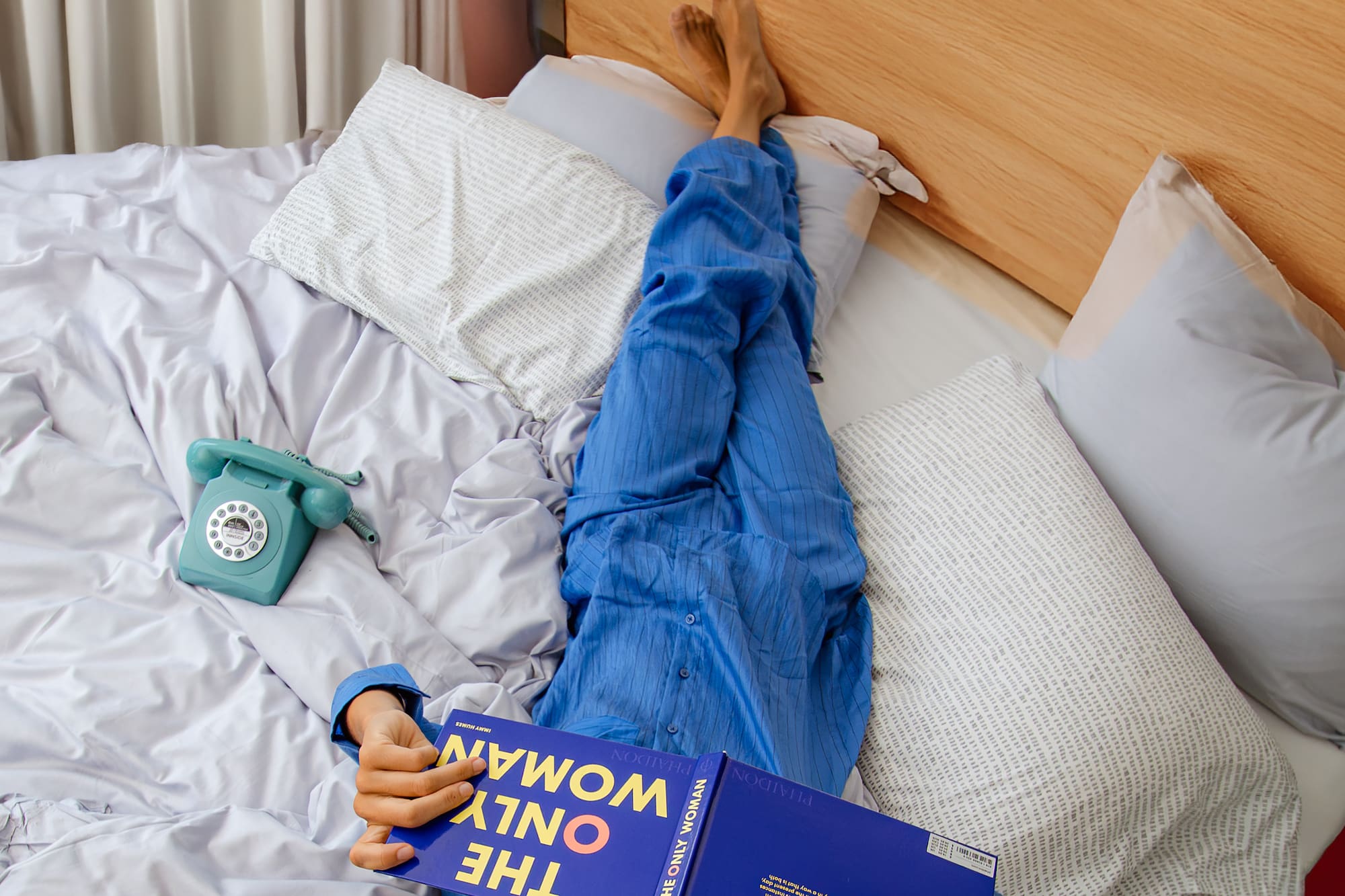 a person lying on a bed with a book and telephone