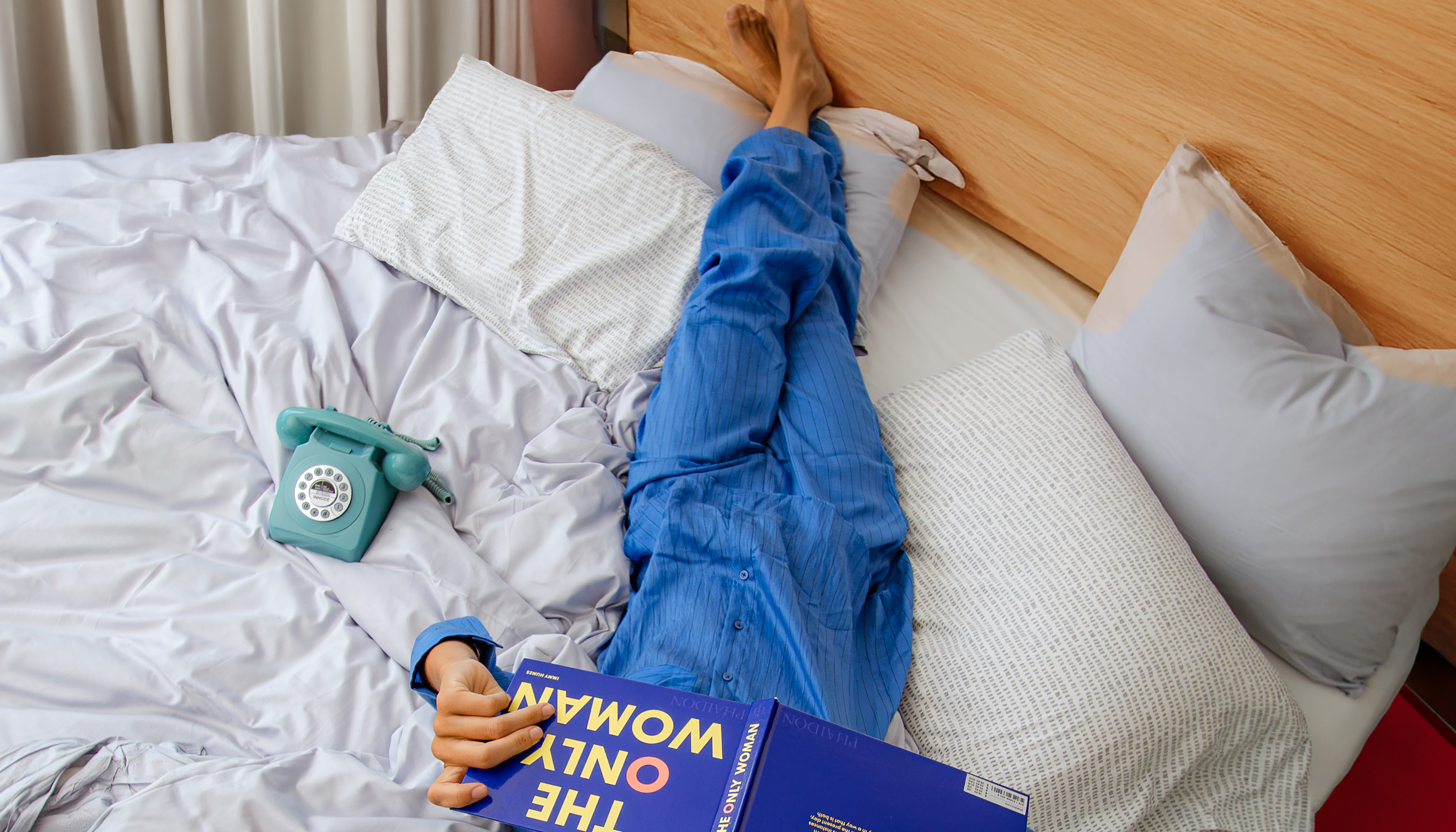 a person lying on a bed with a book and telephone