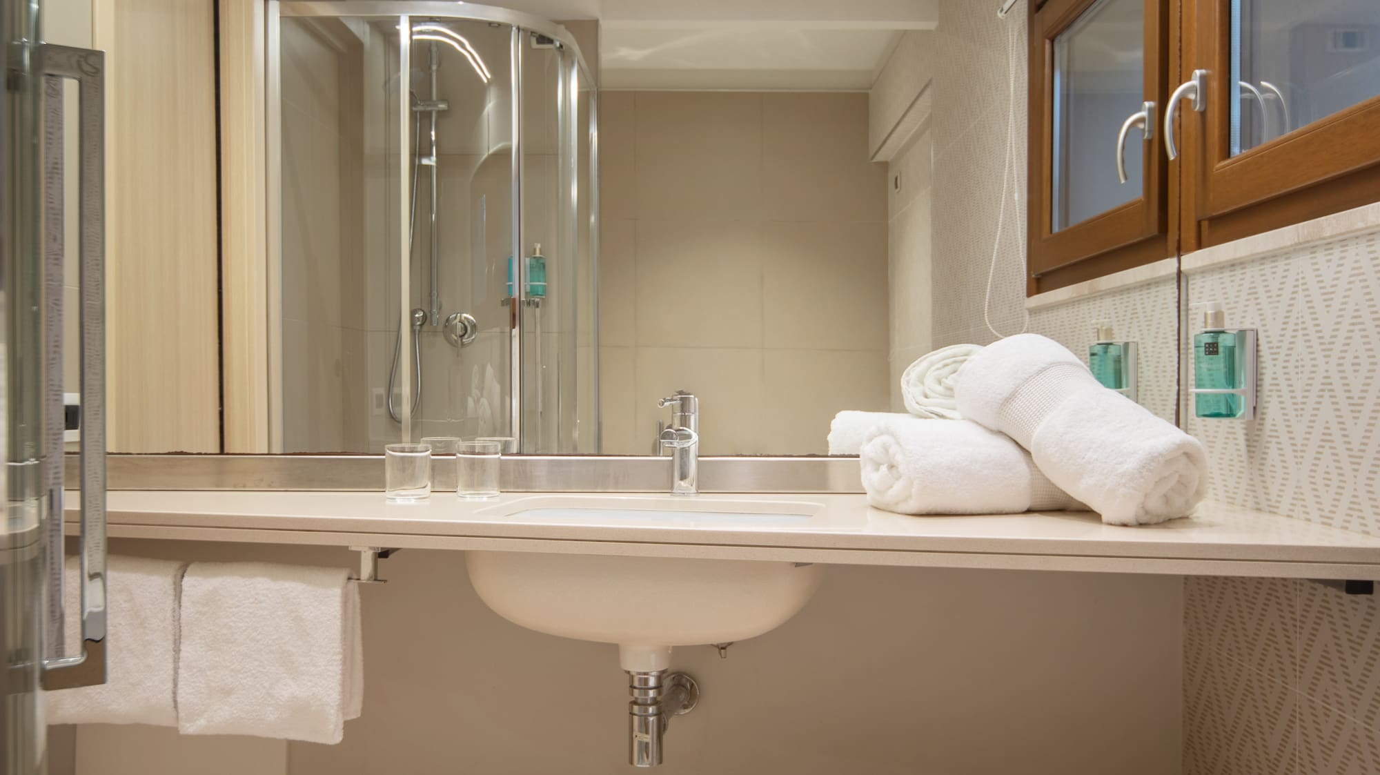 Clean, modern hotel bathroom with sink, mirror, shower, and fresh white towels.
