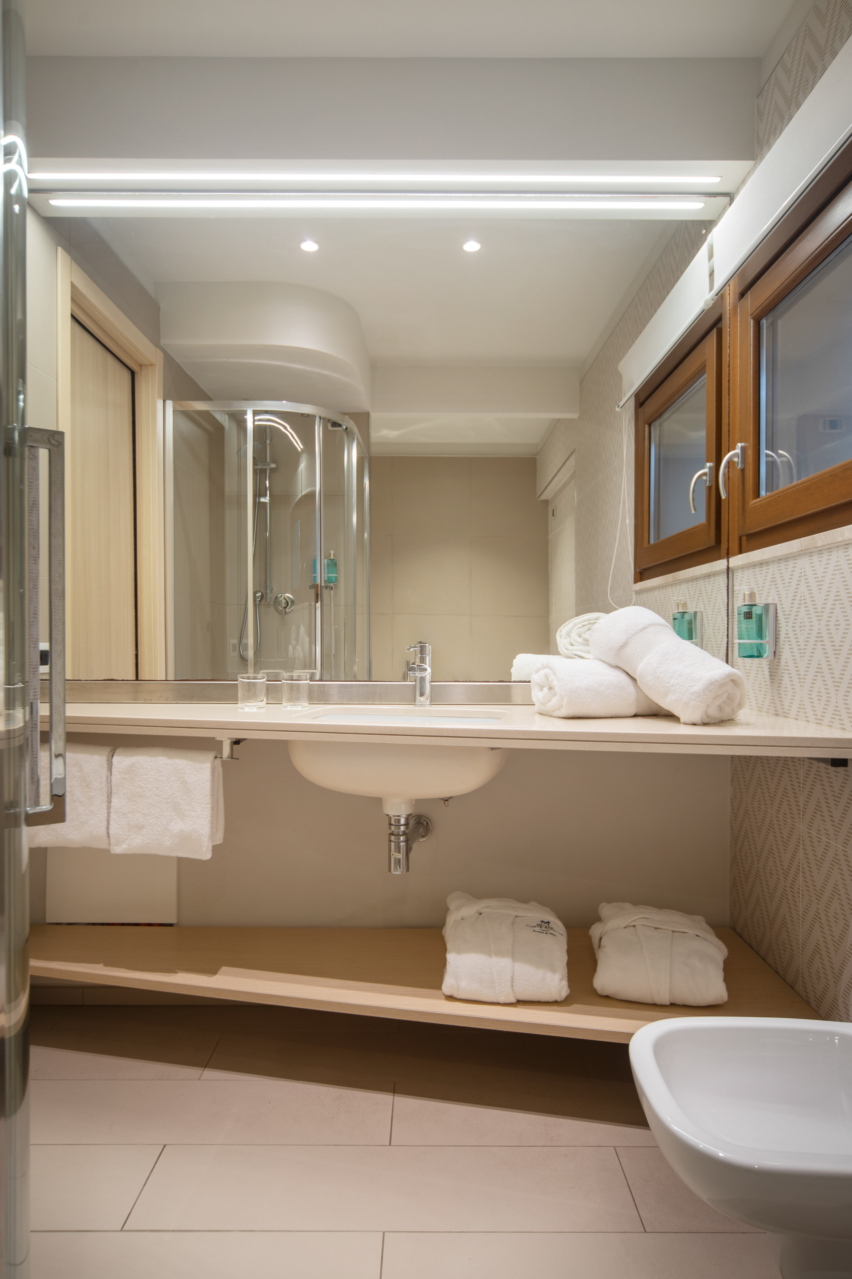 Clean, modern hotel bathroom with sink, mirror, shower, and fresh white towels.