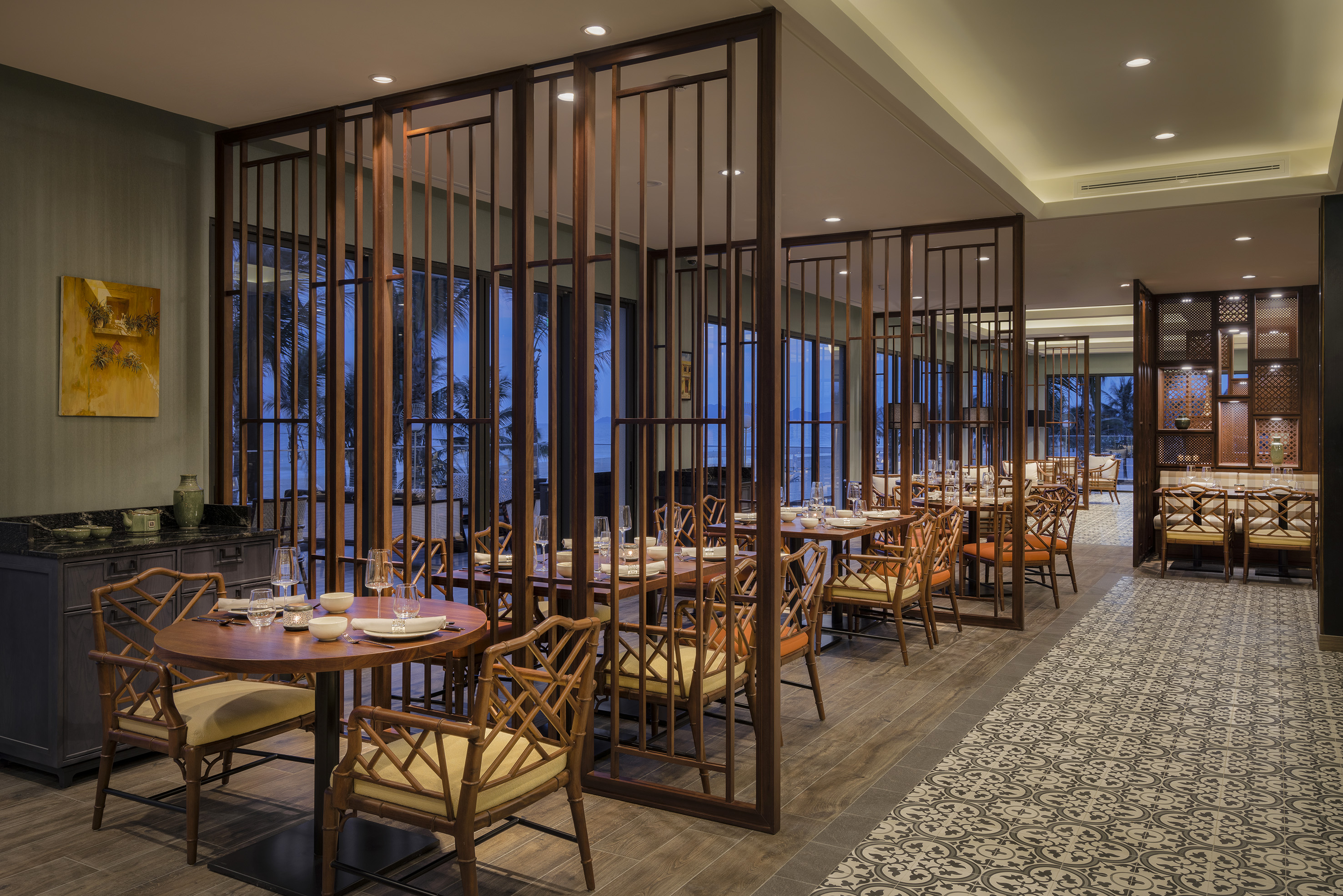 Asian-style restaurant with wooden screens, set tables, and tropical palm tree view.