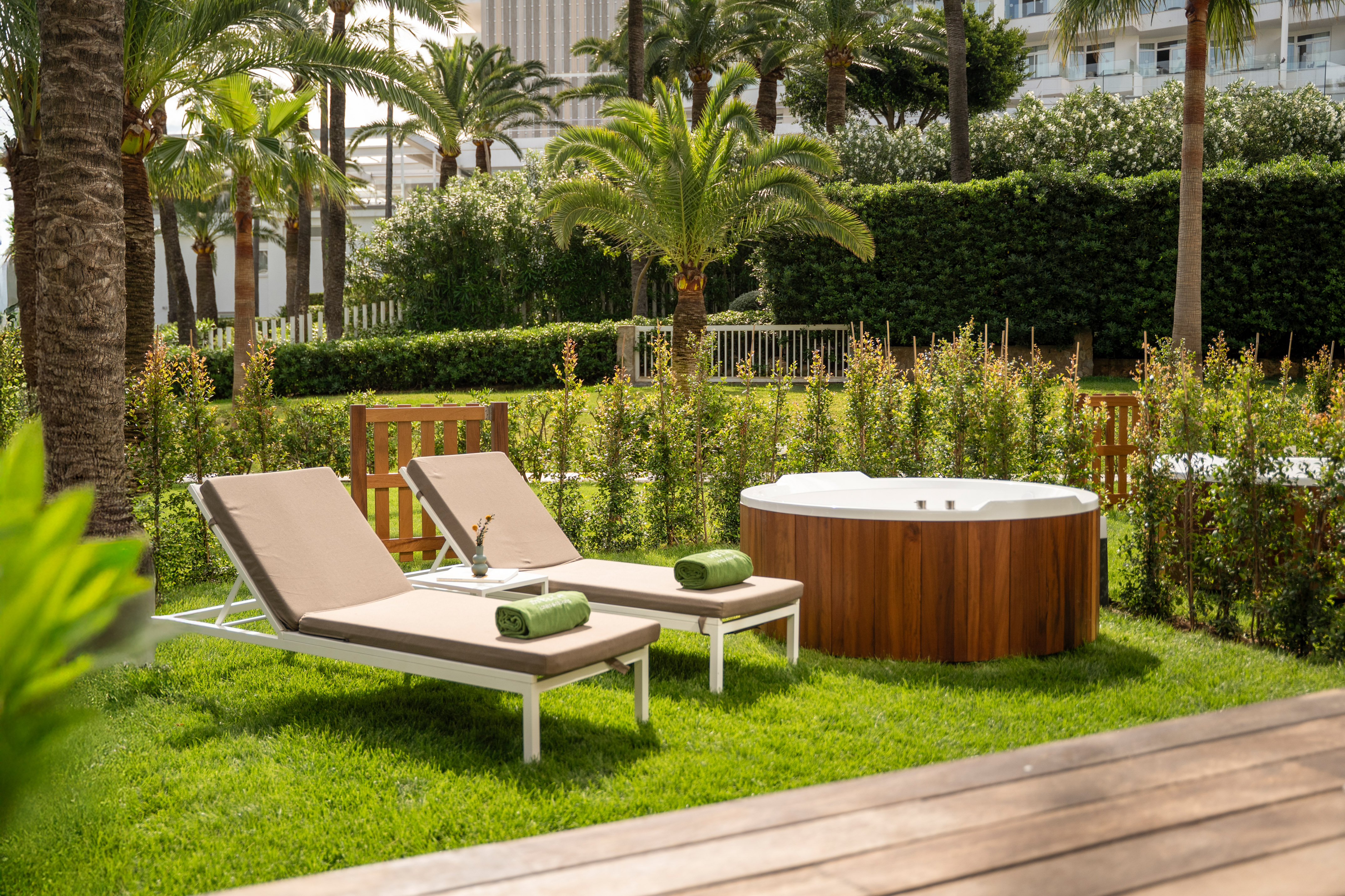 Resort garden with lounge chairs, wooden jacuzzi, and tropical palm trees.