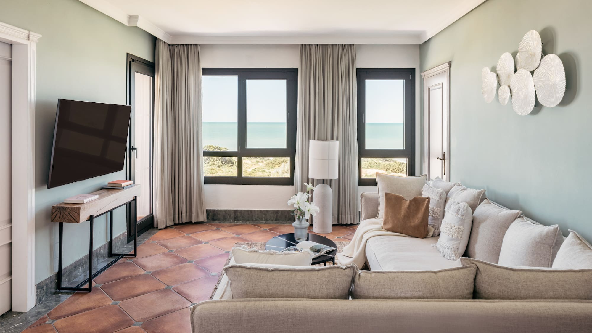 Coastal living room with sea view, light sofa, TV, and terracotta tiles.