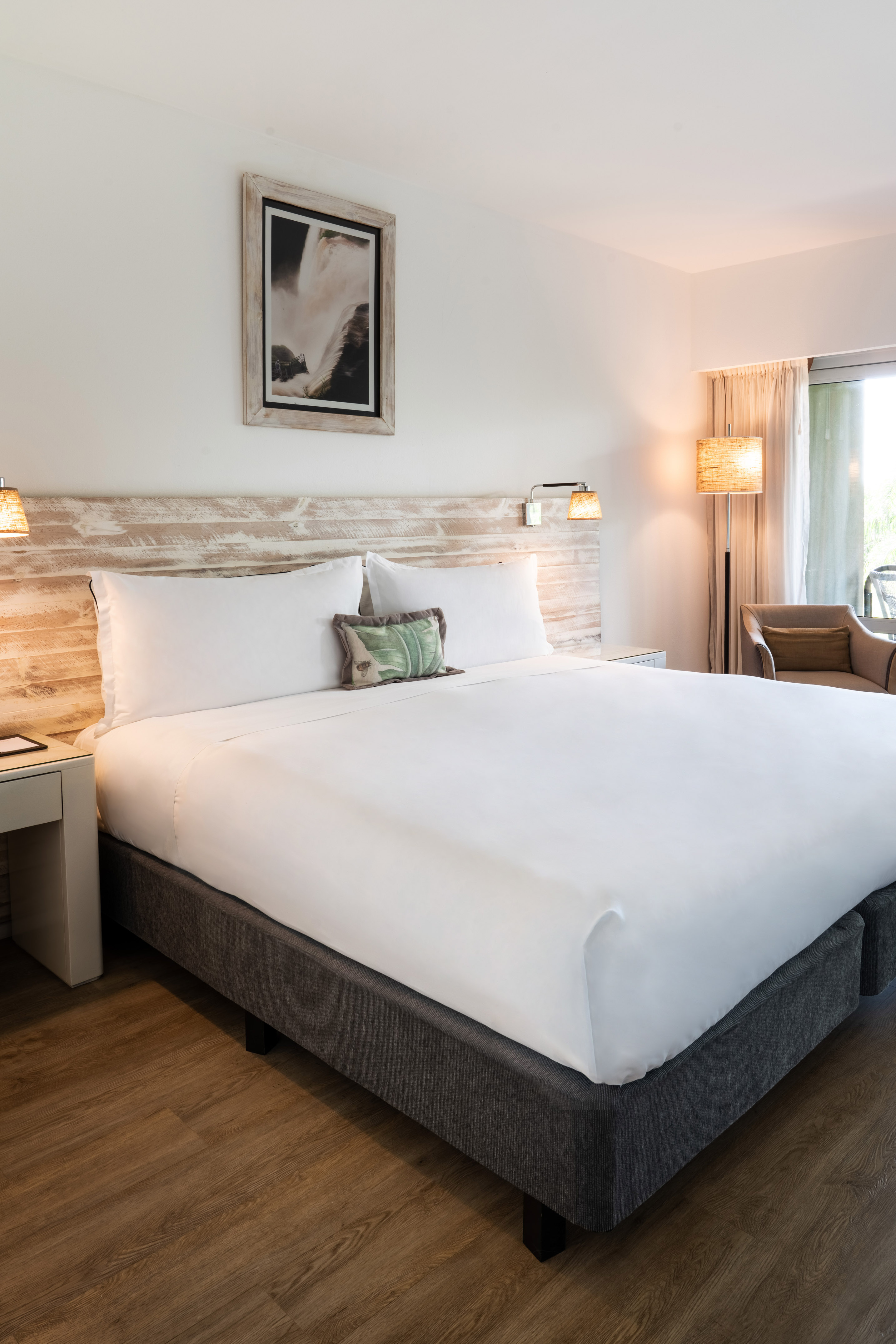 Hotel room with large white bed, rustic wood headboard, and sunlit window.