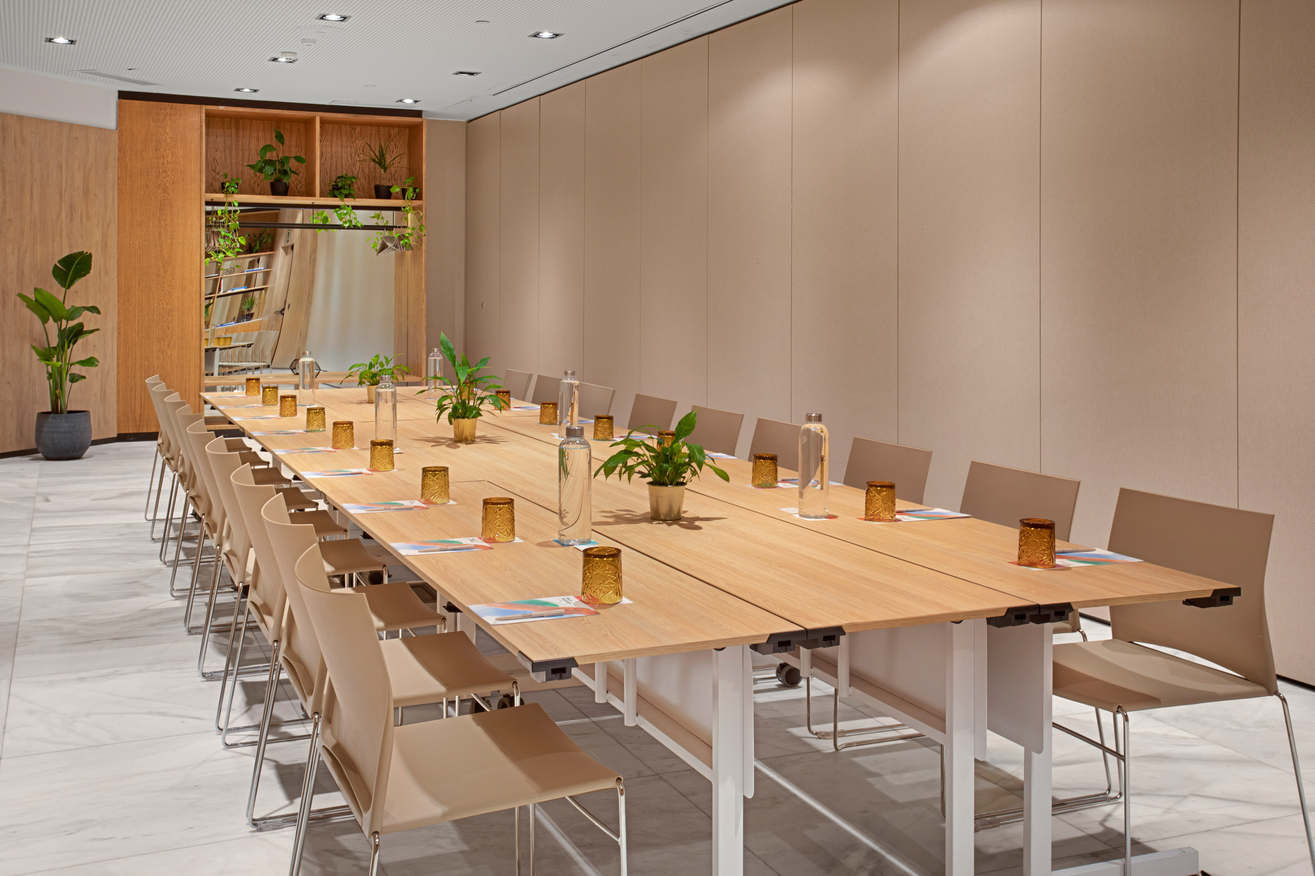 Modern conference room with long wooden table, beige chairs, and potted plants.