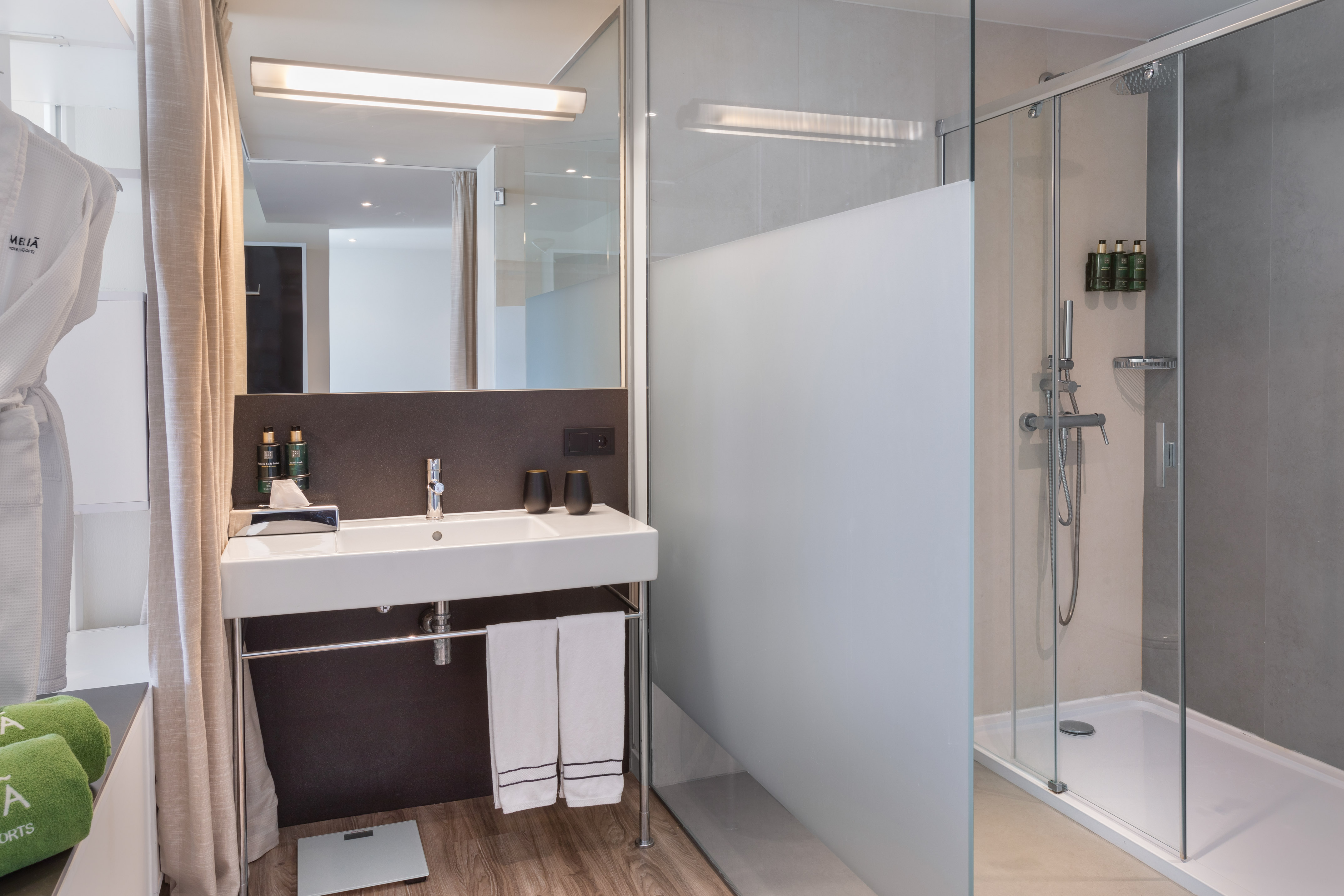Modern hotel bathroom with glass shower, sleek vanity, and mirror.