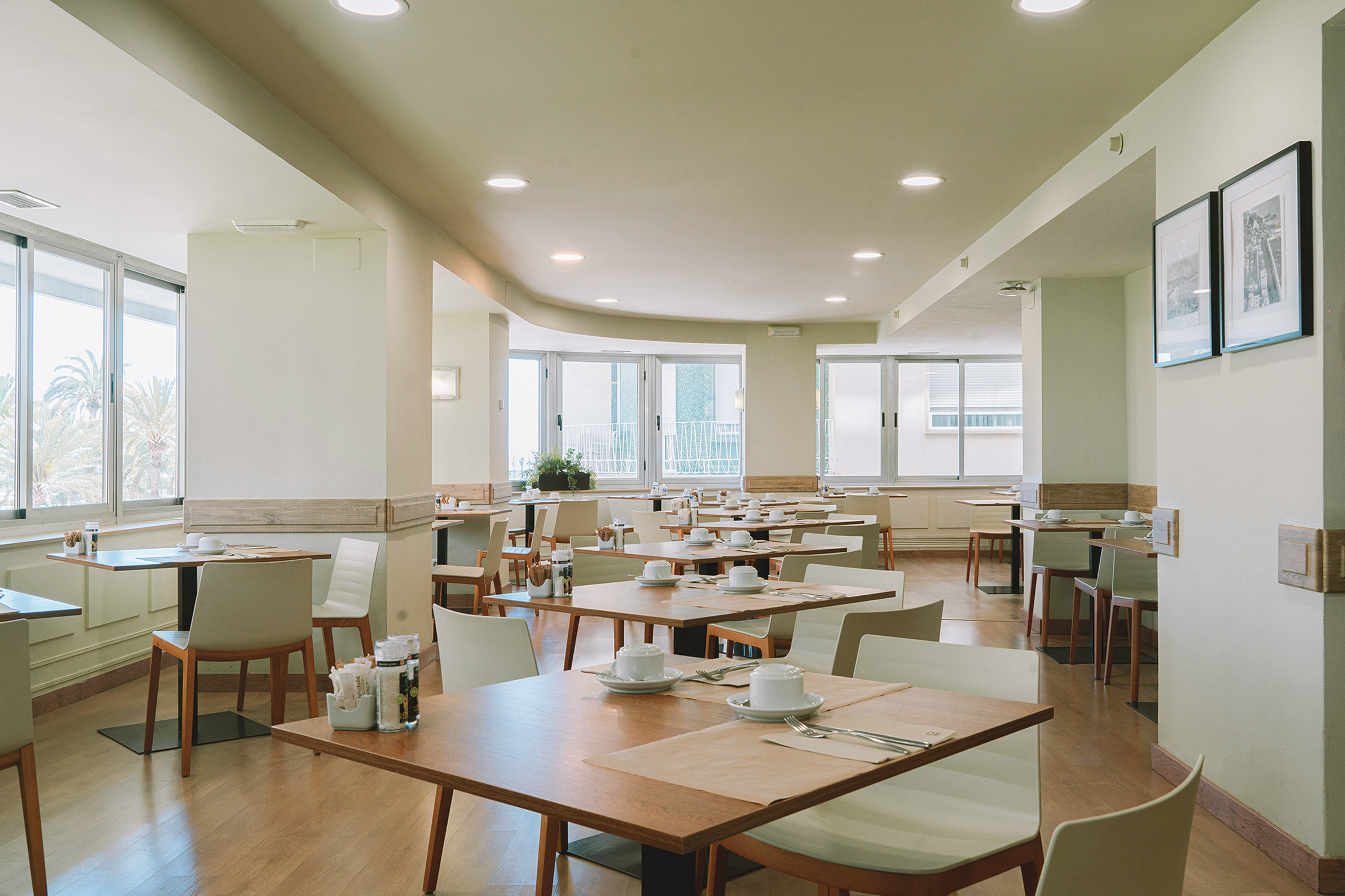 Bright hotel breakfast room with set tables and large windows.