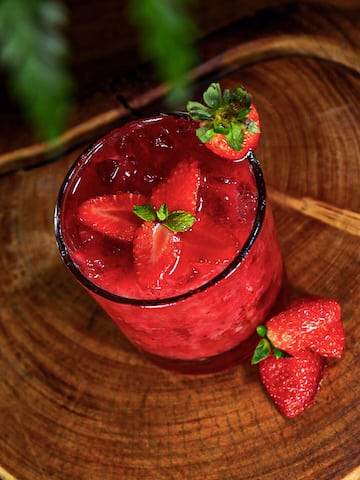 a glass of red drink with strawberries and mint leaves