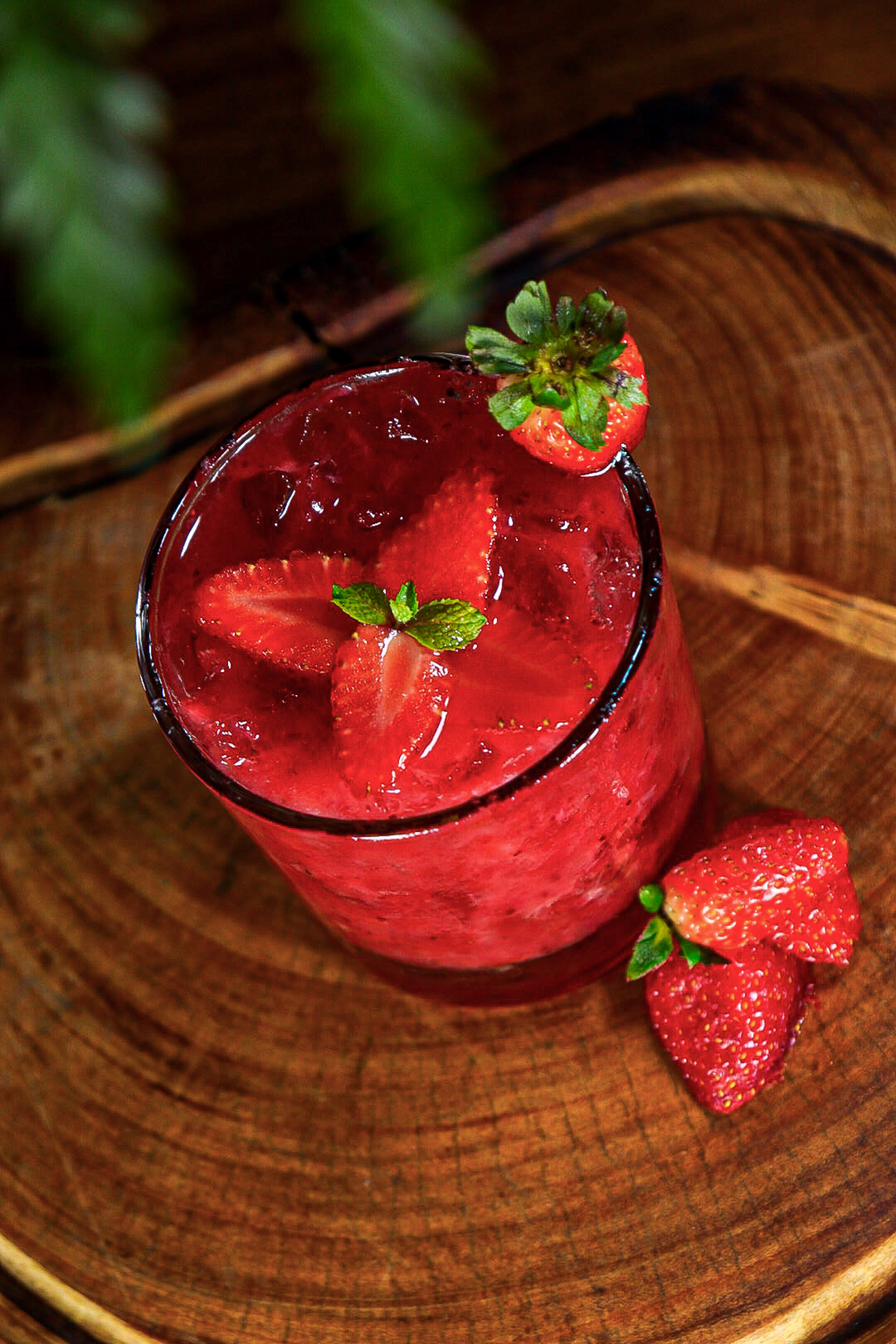 Strawberry drink with fresh strawberries, mint, and ice on a wooden background.