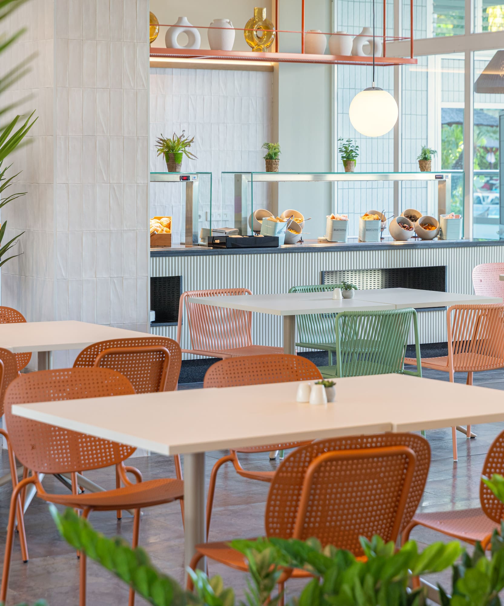 Comedor buffet moderno con mesas, sillas coloridas y plantas.