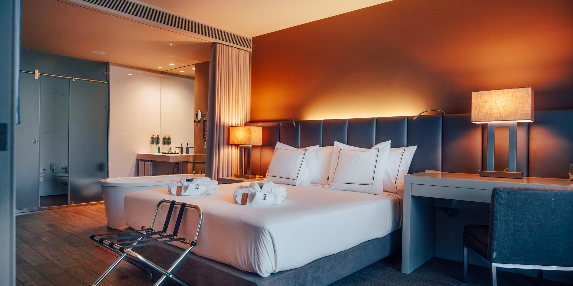 Modern hotel bedroom with king bed, warm lighting, and open concept bath.
