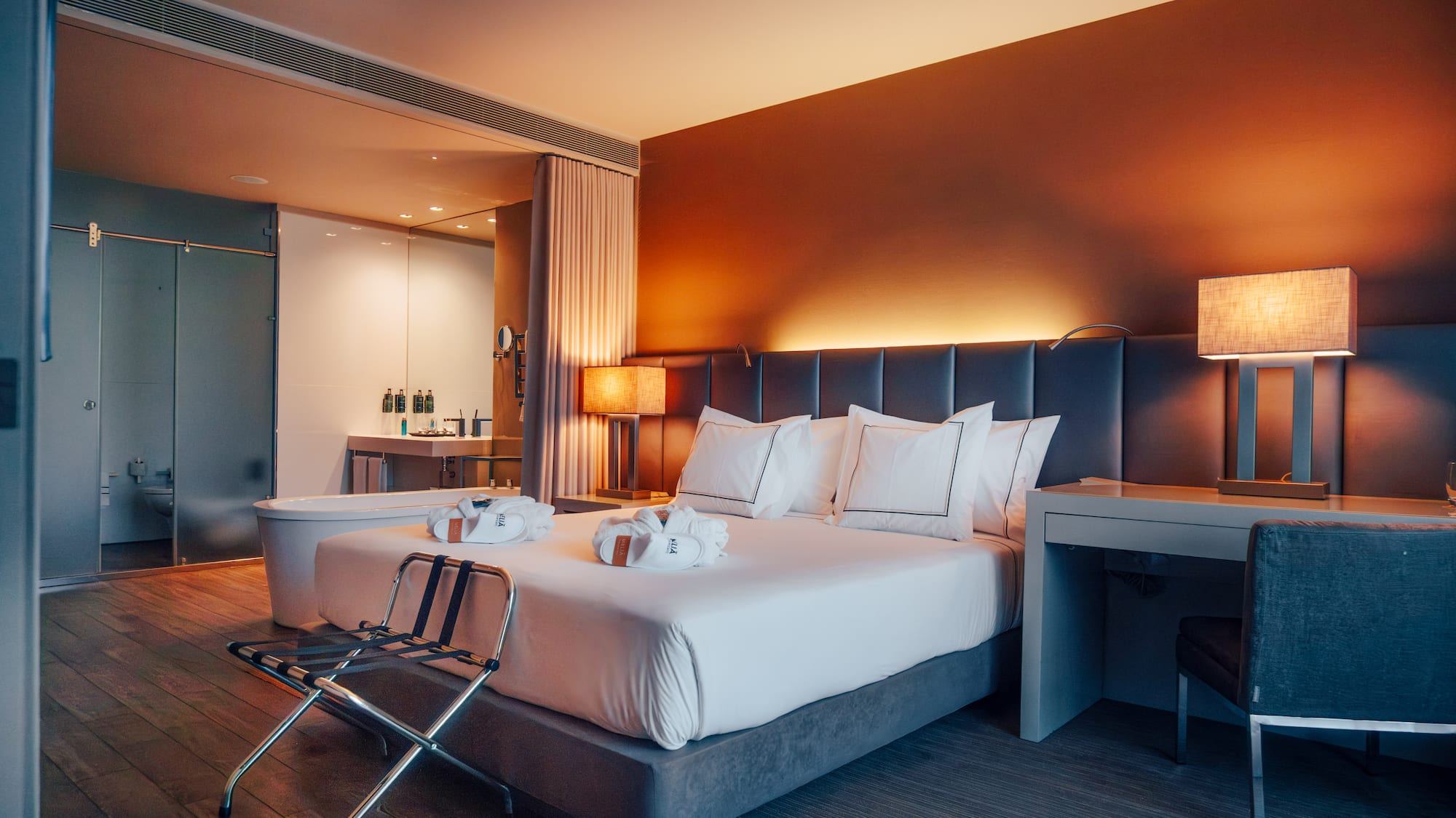 Modern hotel bedroom with king bed, warm lighting, and open concept bath.