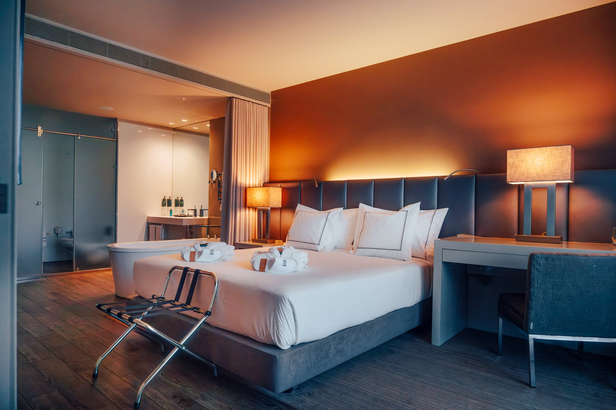 Modern hotel bedroom with king bed, warm lighting, and open concept bath.