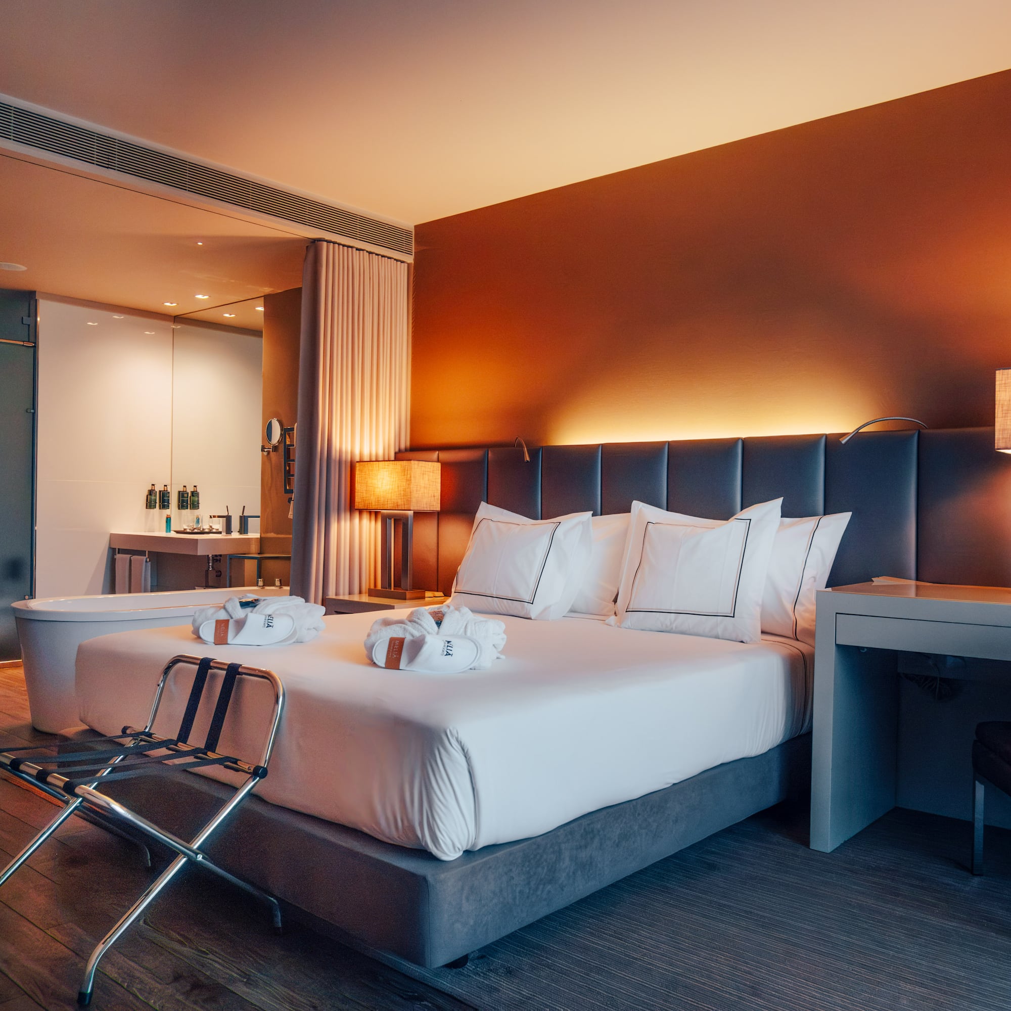 Modern hotel bedroom with king bed, warm lighting, and open concept bath.