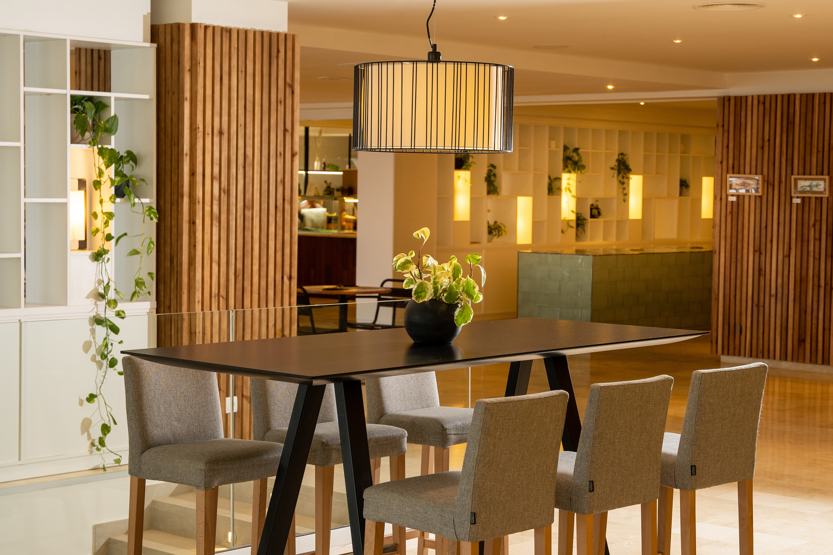 Modern high table with bar stools, plants, and pendant light. Hotel interior.