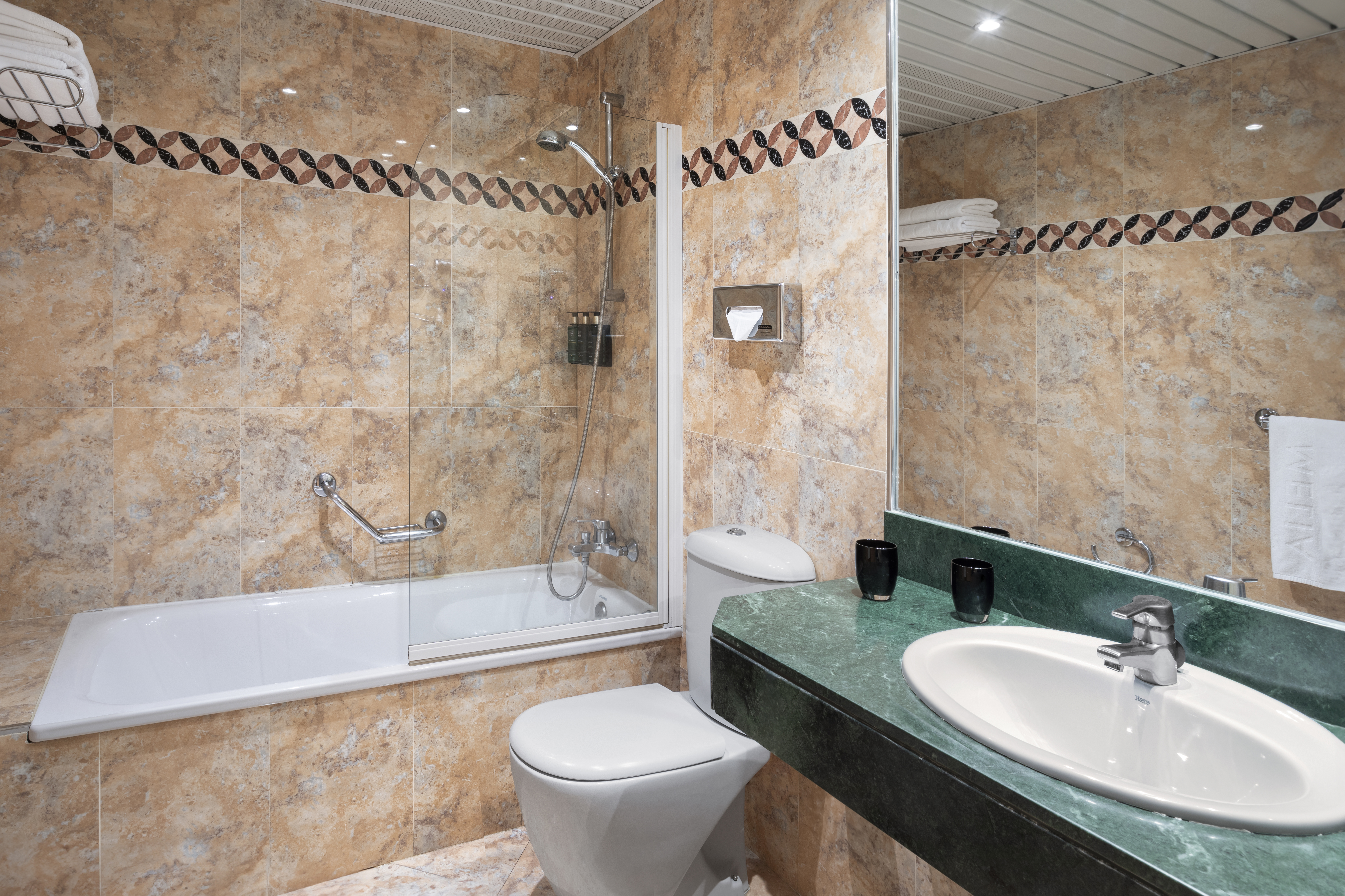 Hotel bathroom with marble-look tiles, bathtub, shower, toilet, green sink.