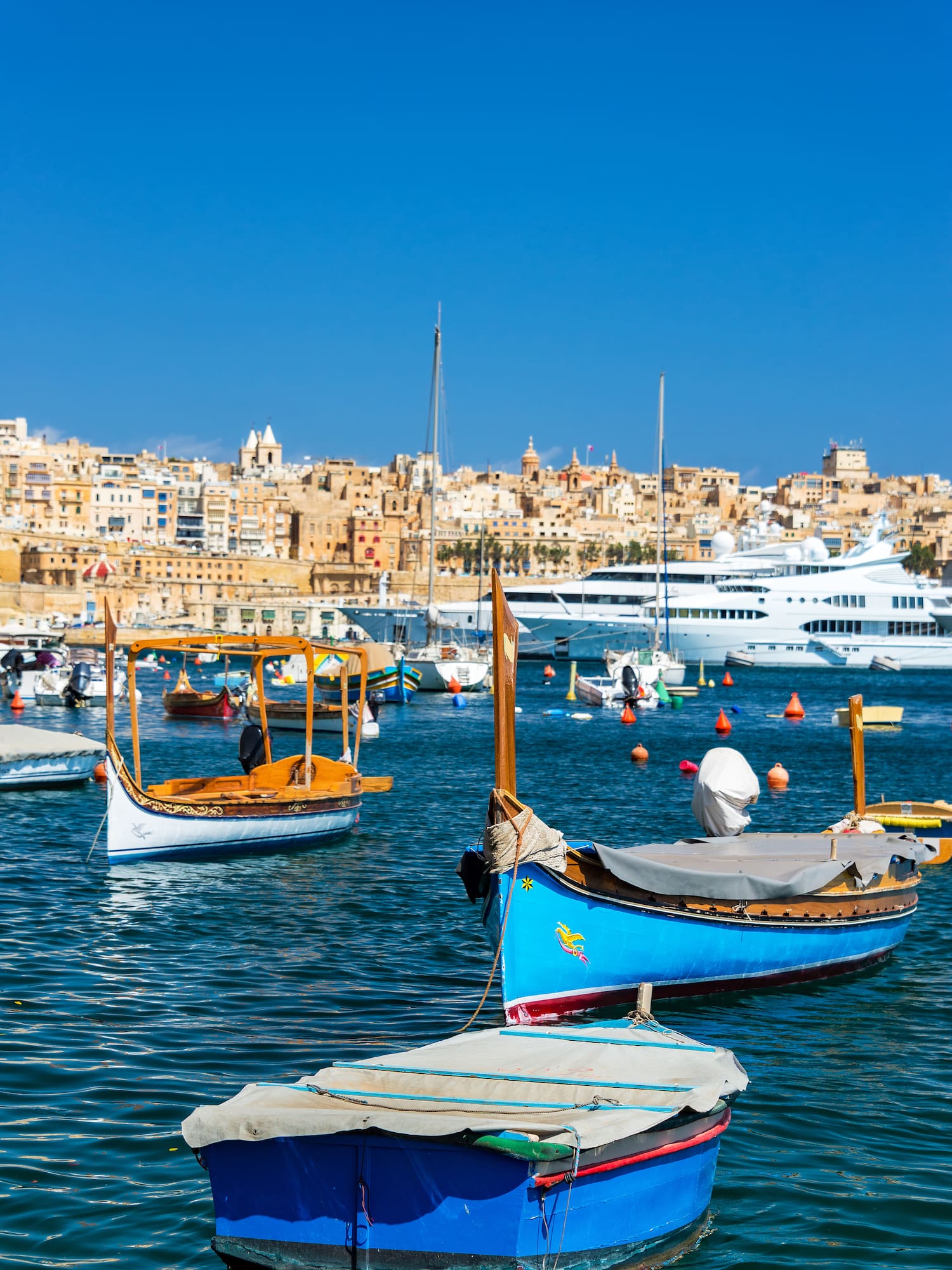 Traditional Maltese luzzu boats in Valletta harbor with historic cityscape.