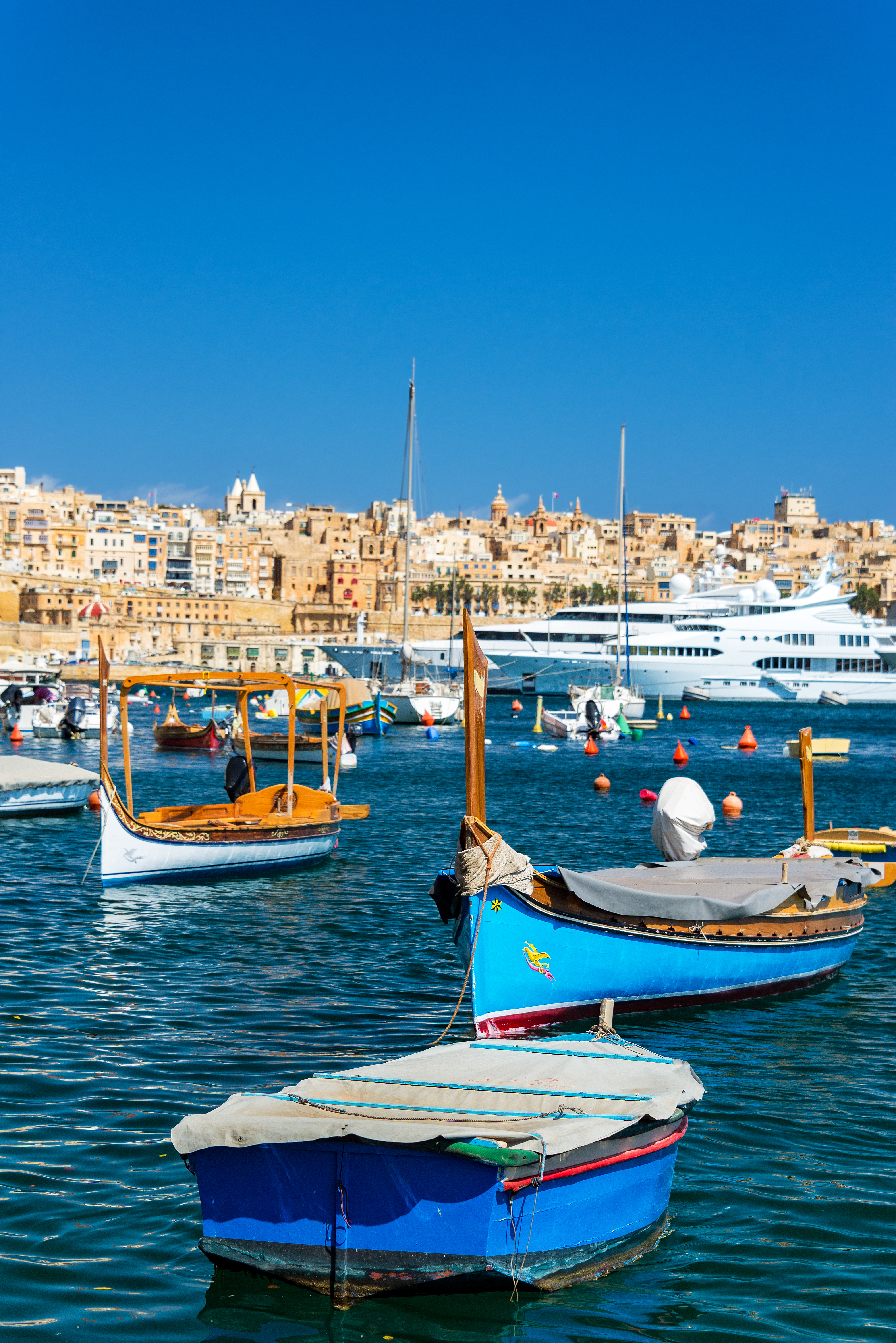 Traditional Maltese luzzu boats in Valletta harbor with historic cityscape.