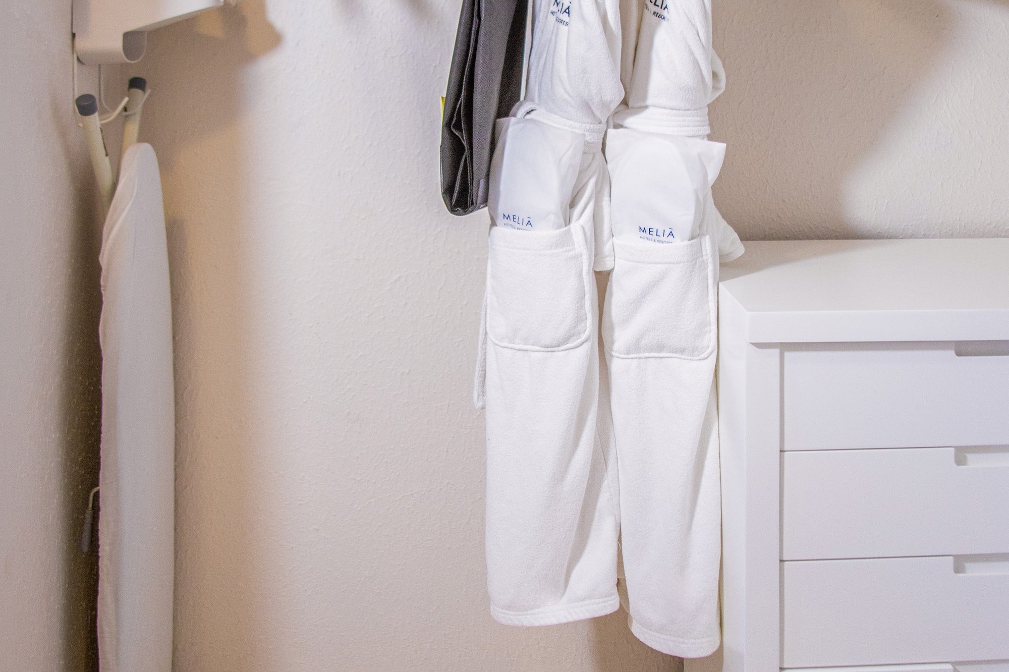 Hotel closet with Meliã bathrobes, iron, ironing board, safe, and white dresser.