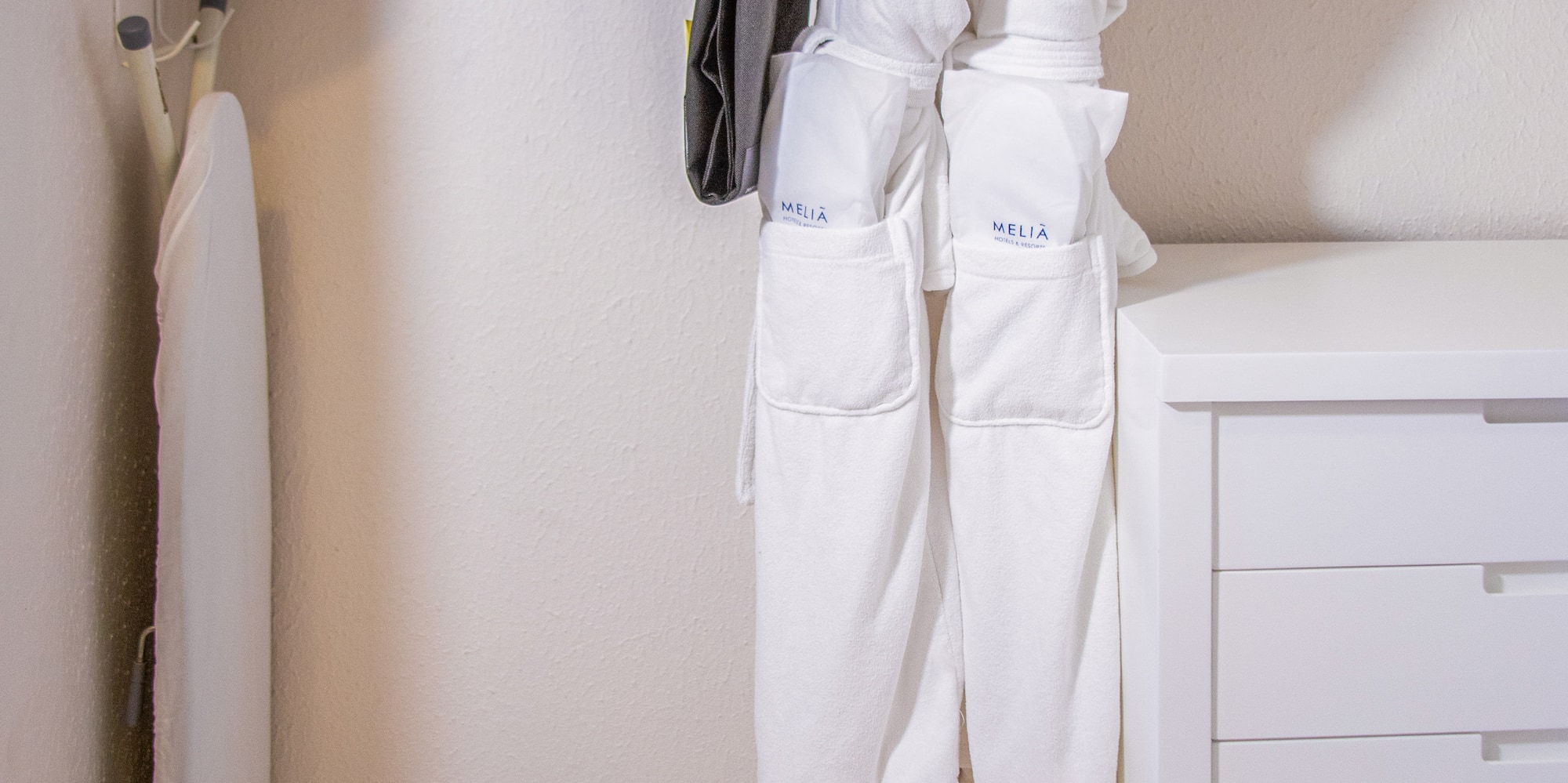 Hotel closet with Meliã bathrobes, iron, ironing board, safe, and white dresser.