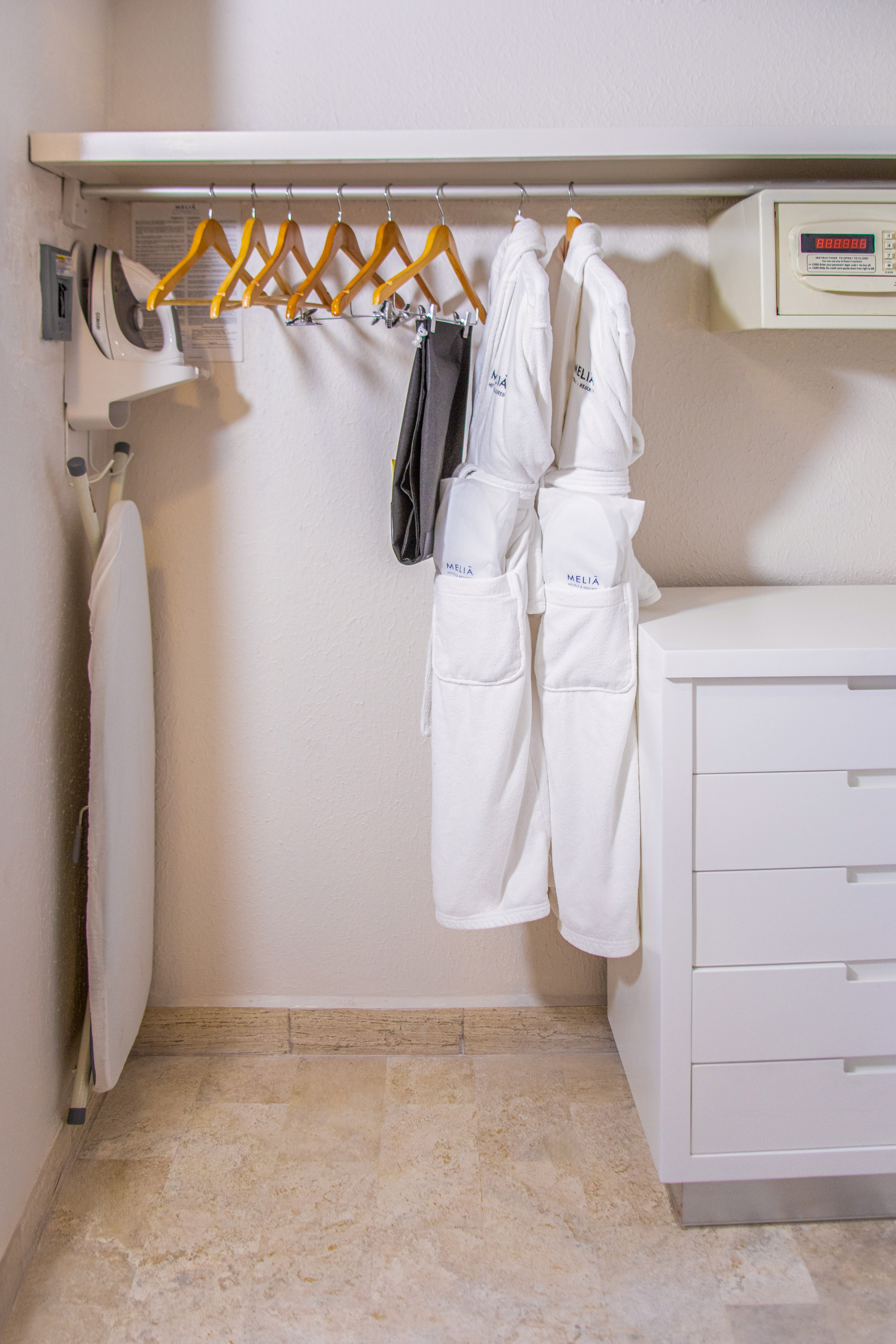 Hotel closet with Meliã bathrobes, iron, ironing board, safe, and white dresser.