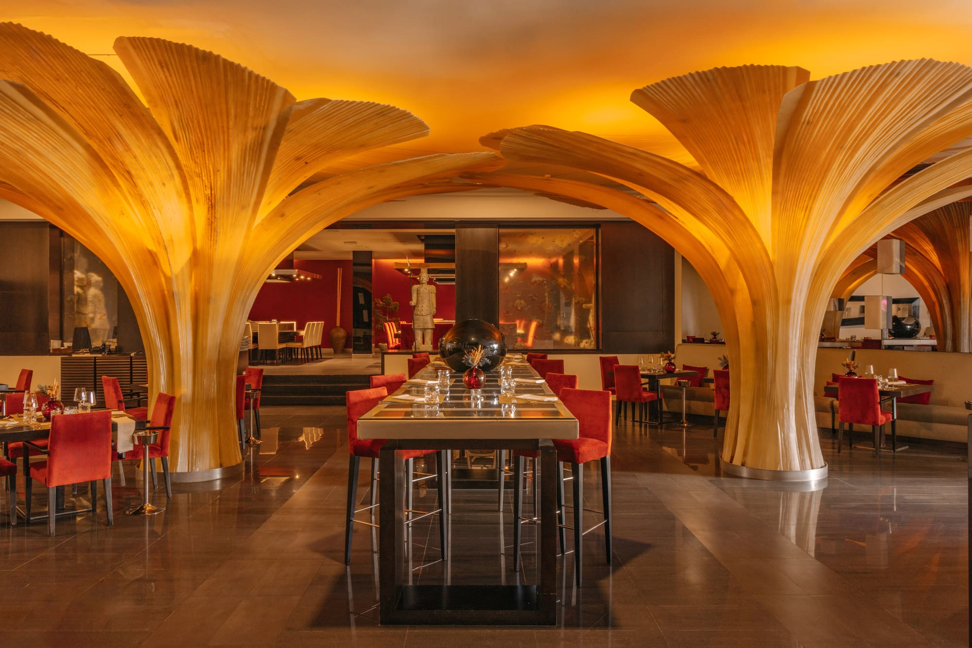 Modern restaurant with artistic wooden arches, amber lighting, and red chairs.