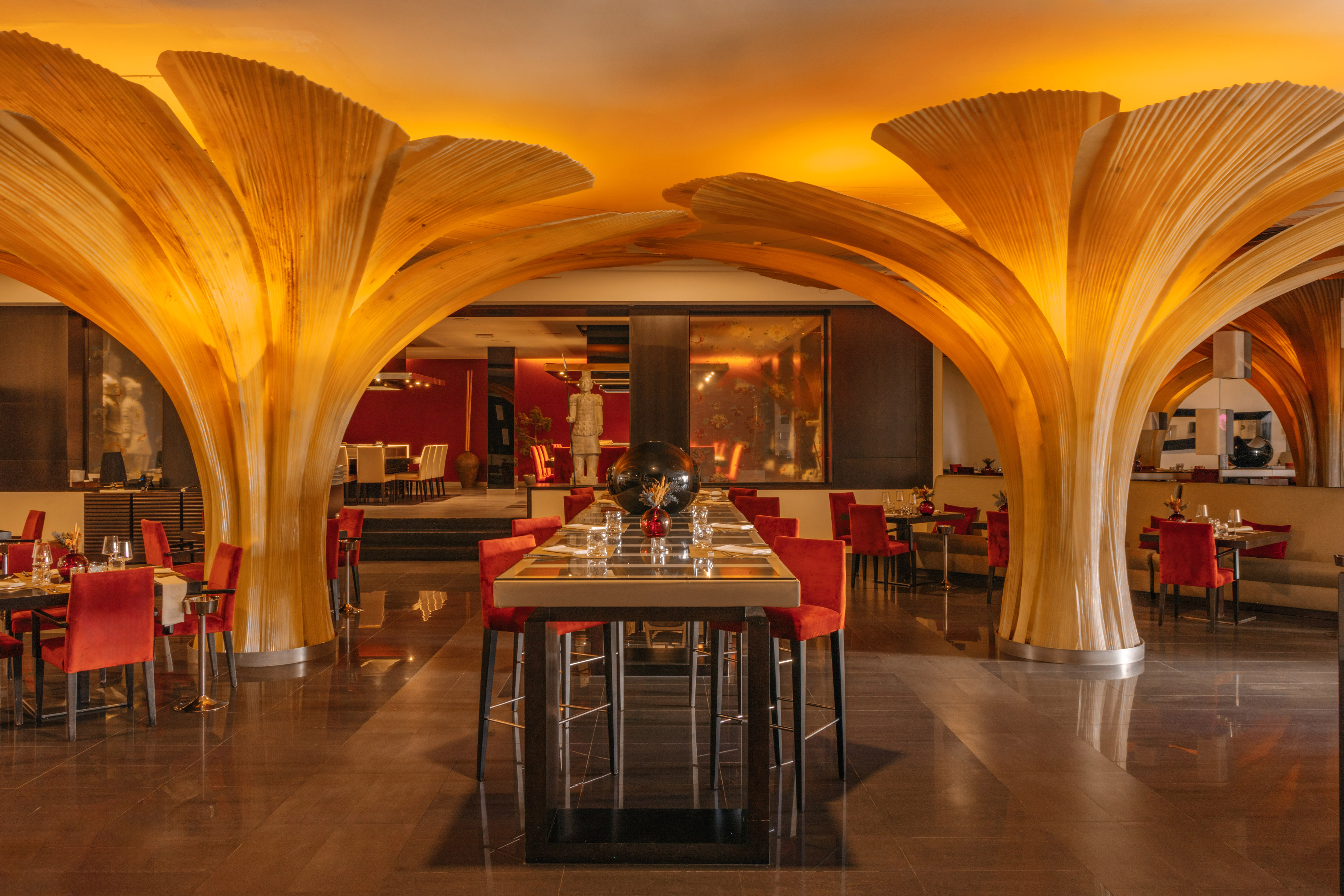Modern restaurant with artistic wooden arches, amber lighting, and red chairs.