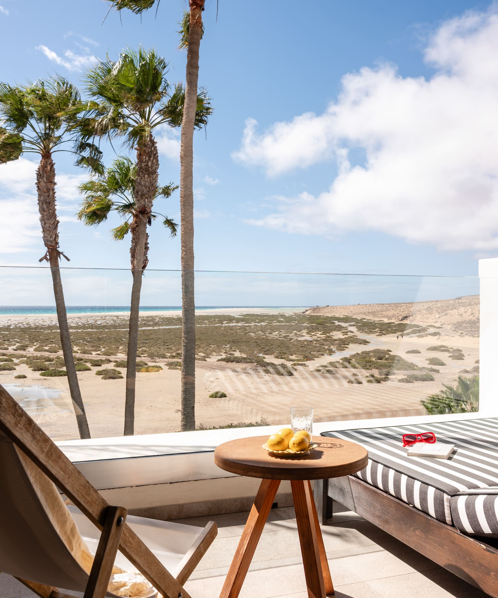 Sunny balcony overlooking a tropical beach with palm trees and a comfortable sun lounger.