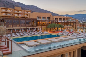 Luxury resort with large swimming pool, sun loungers, and mountain view, evening.