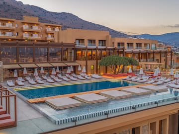 Luxury resort with large swimming pool, sun loungers, and mountain view, evening.