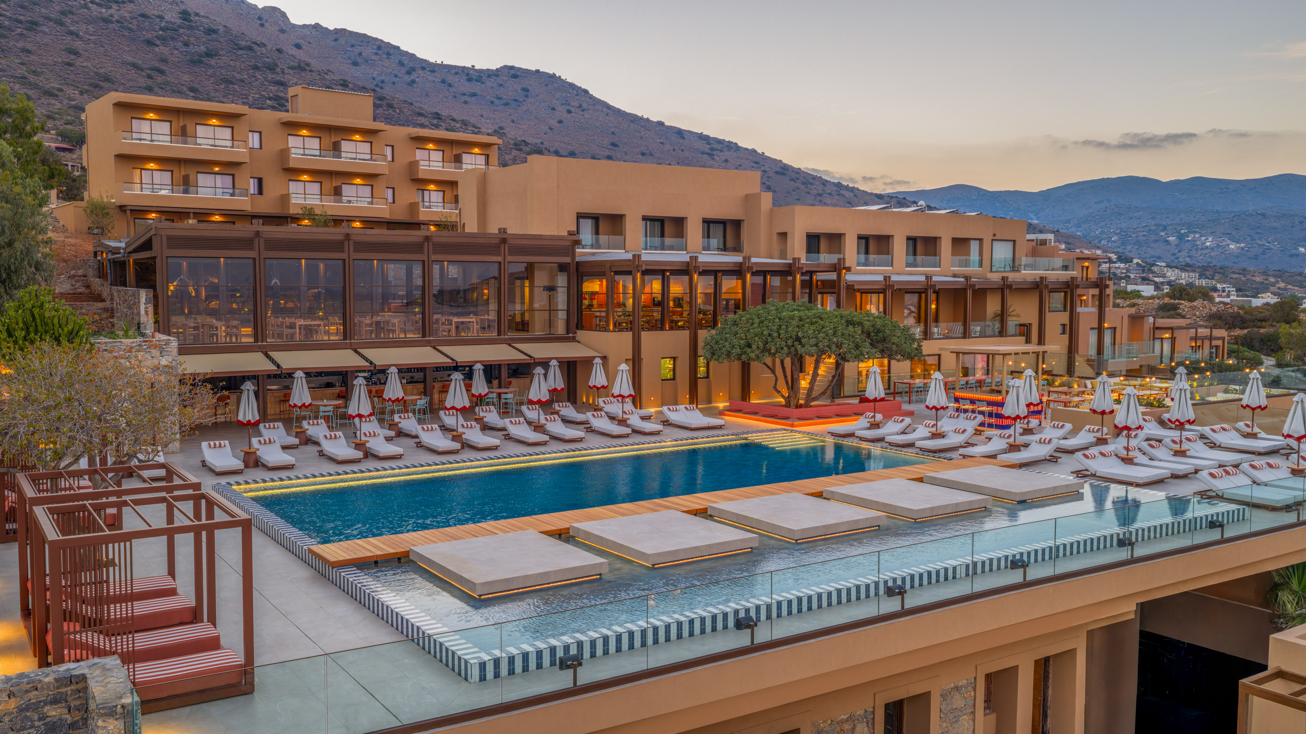 Luxury hotel resort pool with lounge chairs, umbrellas, and mountains at dusk.