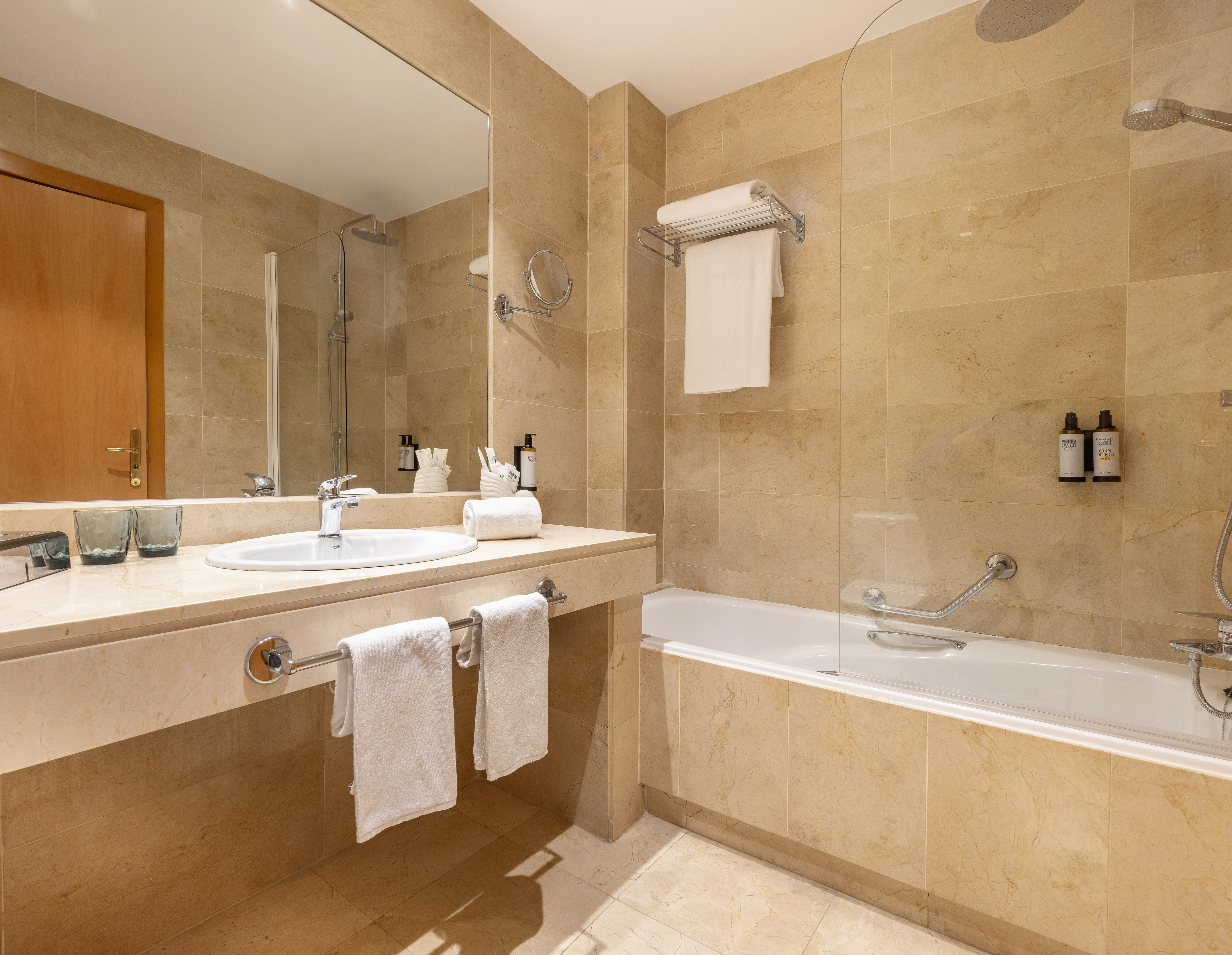 Modern hotel bathroom with beige marble, white sink, bathtub, and shower.