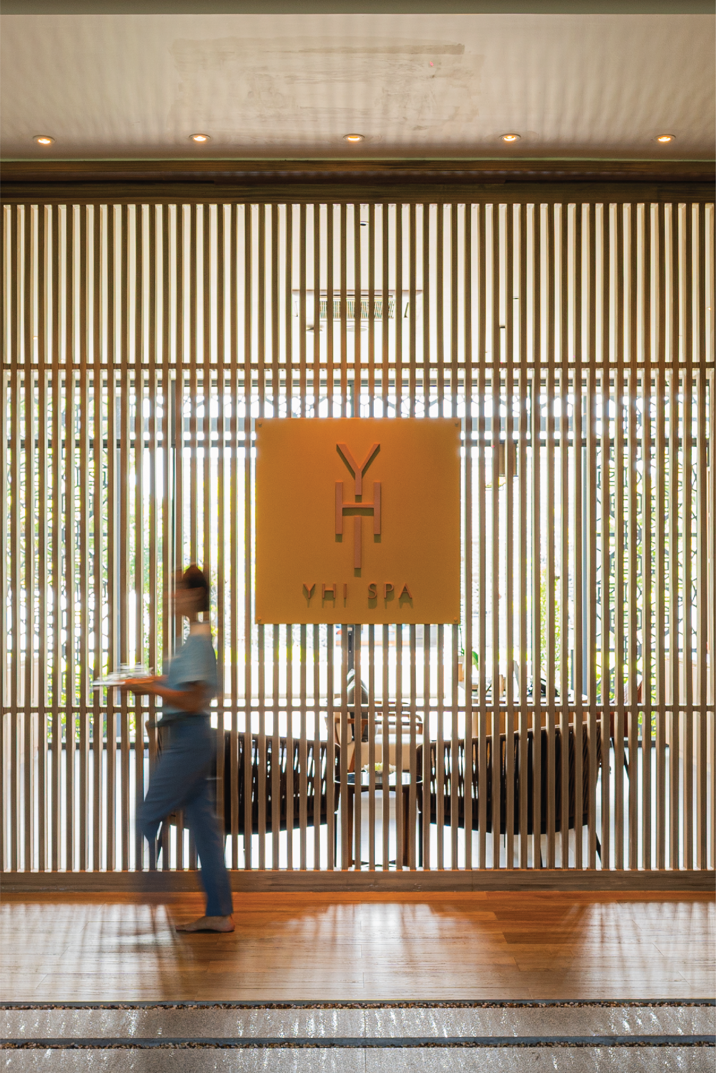 Modern YHI SPA reception, slatted wood screen, staff with tray.