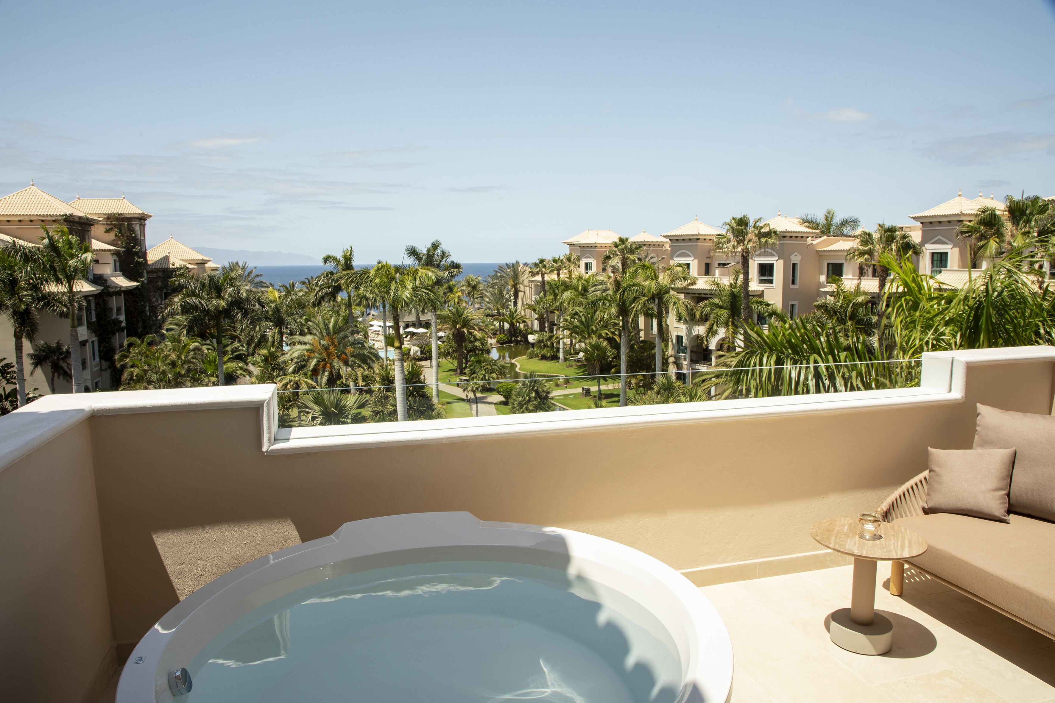 Luxury resort balcony with hot tub, ocean view, and palm trees.
