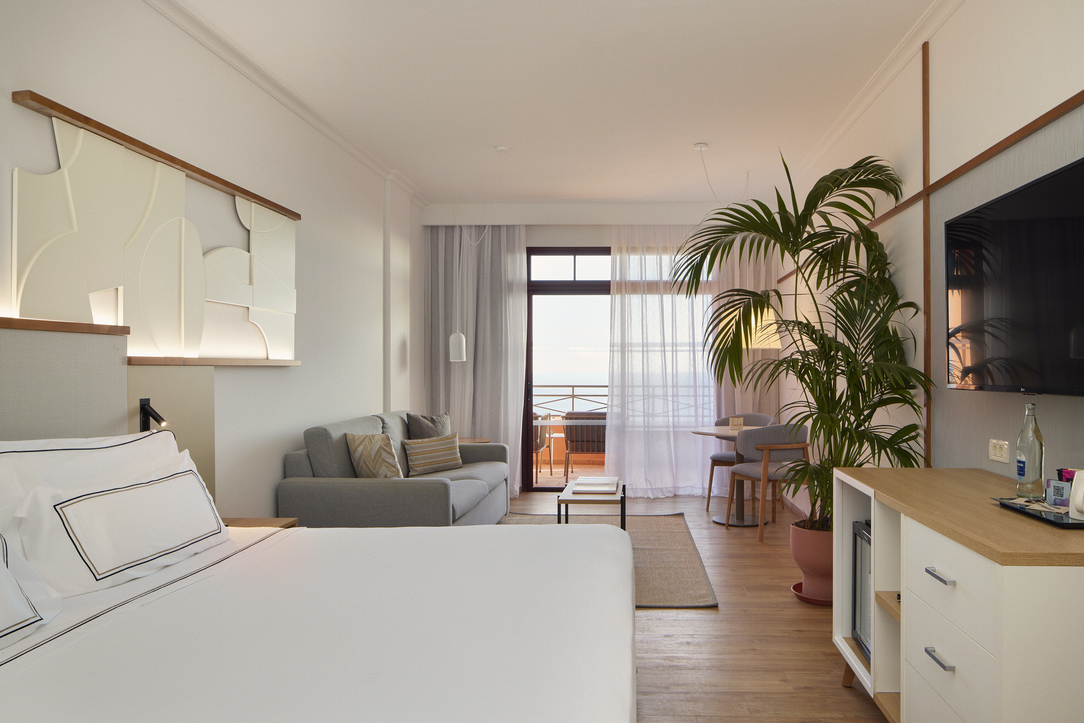 Modern hotel suite with bed, living area, and ocean view balcony.
